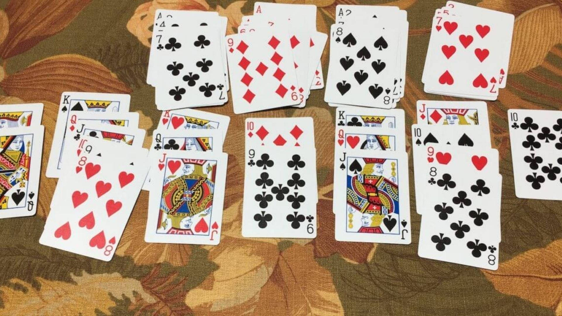 Solitaire遊戲精彩瞬間 壁紙 — 散落的紅色和黑色花式啤牌放在有圖案的棕色和米色布料表面上。