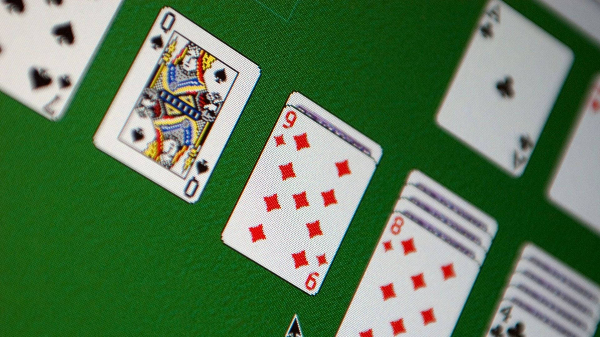 Solitaire電腦遊戲 壁紙 — 啤牌散落在綠色絨面枱上的特寫，焦點清晰對準黑桃皇后和方塊九。