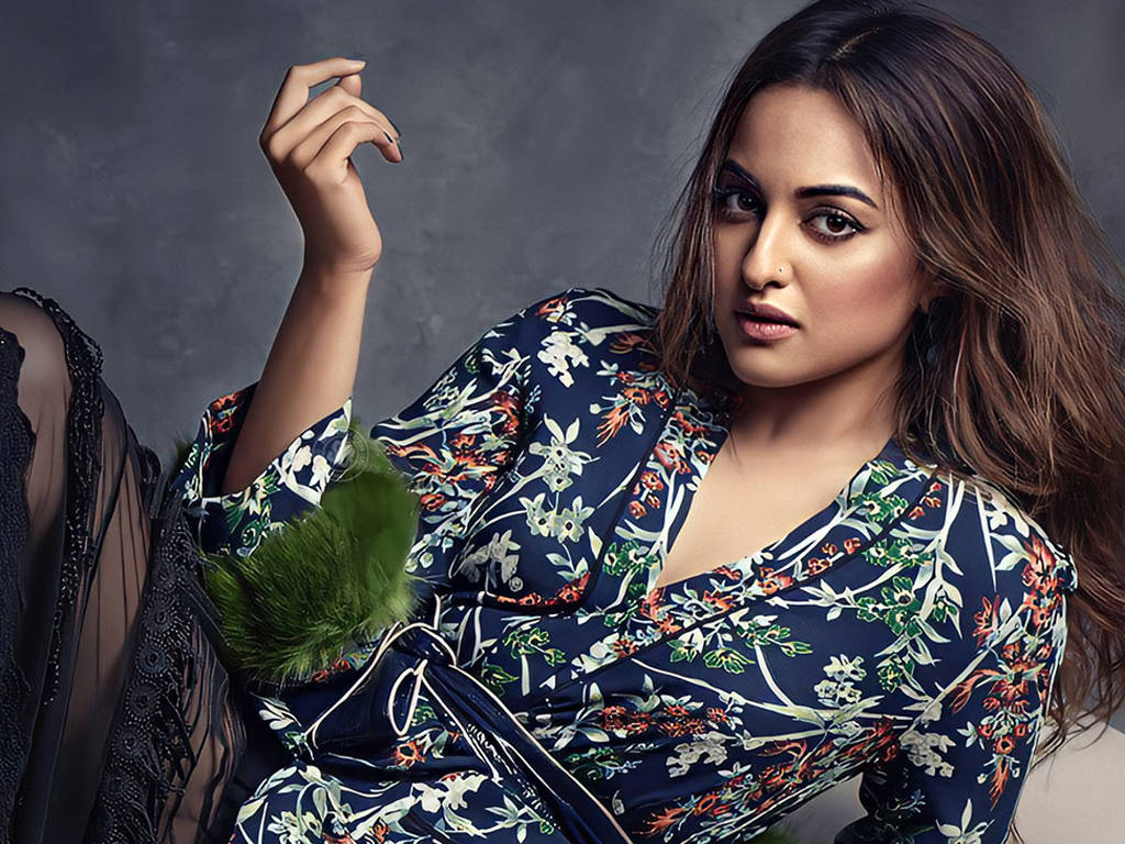 Sonakshi Sinha 時尚浴袍造型 壁紙 — 一位身穿海軍藍花卉連衣裙、搭配綠色毛皮裝飾的女性，在紋理灰色背景前自信地擺姿勢。