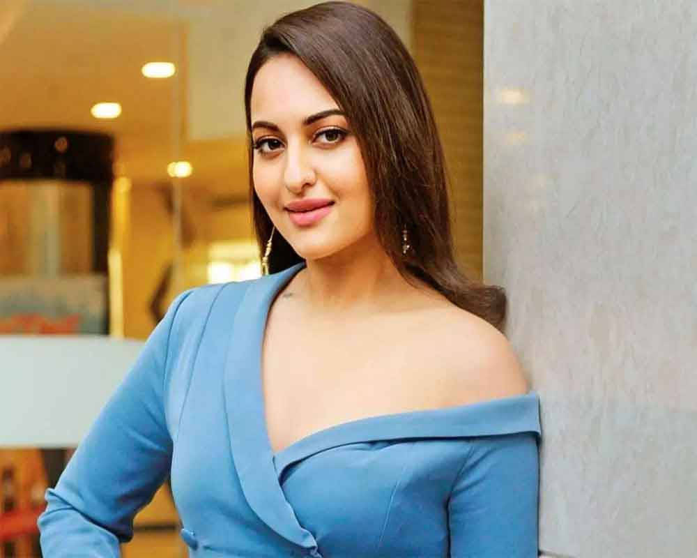 Sonakshi Sinha 漂亮臉龐 壁紙 — 一位身穿藍色露肩連衣裙的女性靠在牆上，身後有溫暖的室內燈光。