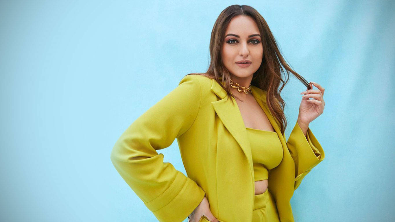 Sonakshi Sinha 苹果綠服裝造型 壁紙 — 一位身穿大膽黃色西裝外套和配套上衣的女性，在柔和的藍色工作室背景前自信地擺姿勢。