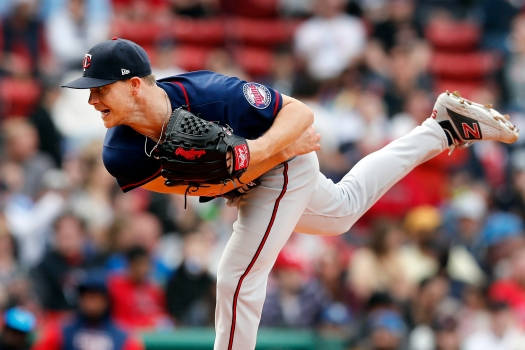 Sonny Gray 投球後的姿態 壁紙 — 一名棒球投手正處於投球動作中，腿部高抬，左手戴著手套，背景是模糊的體育場人群。