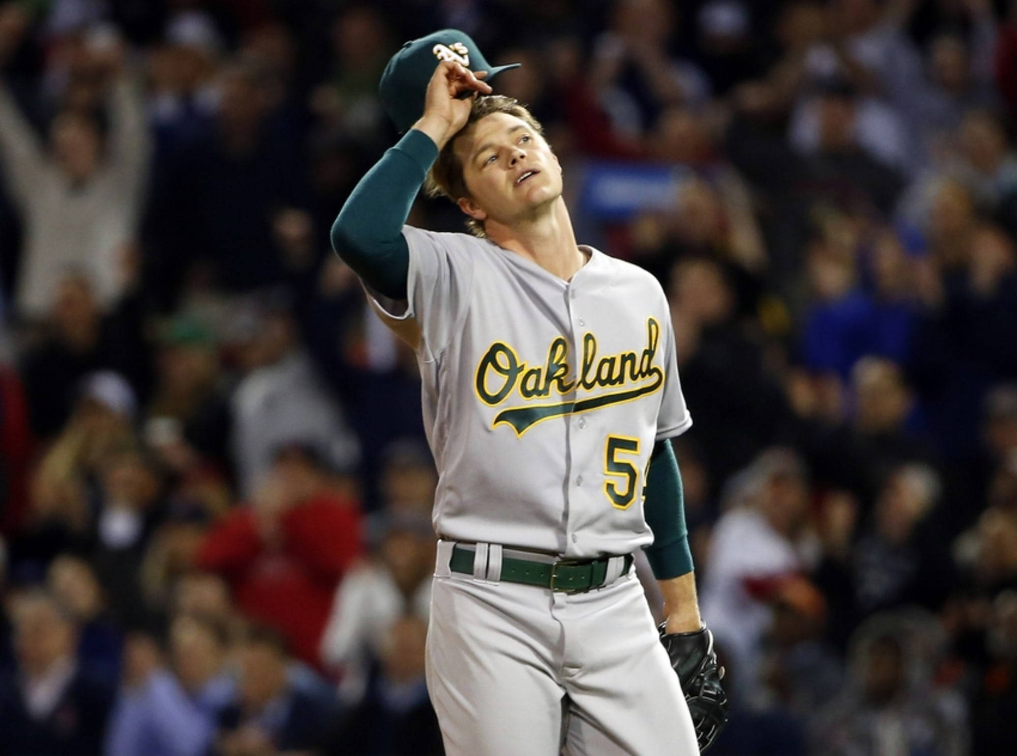 Sonny Gray 摘下帽子 壁紙 — 身穿奧克蘭隊服的棒球手在明亮燈光下的球場內舉起帽子。