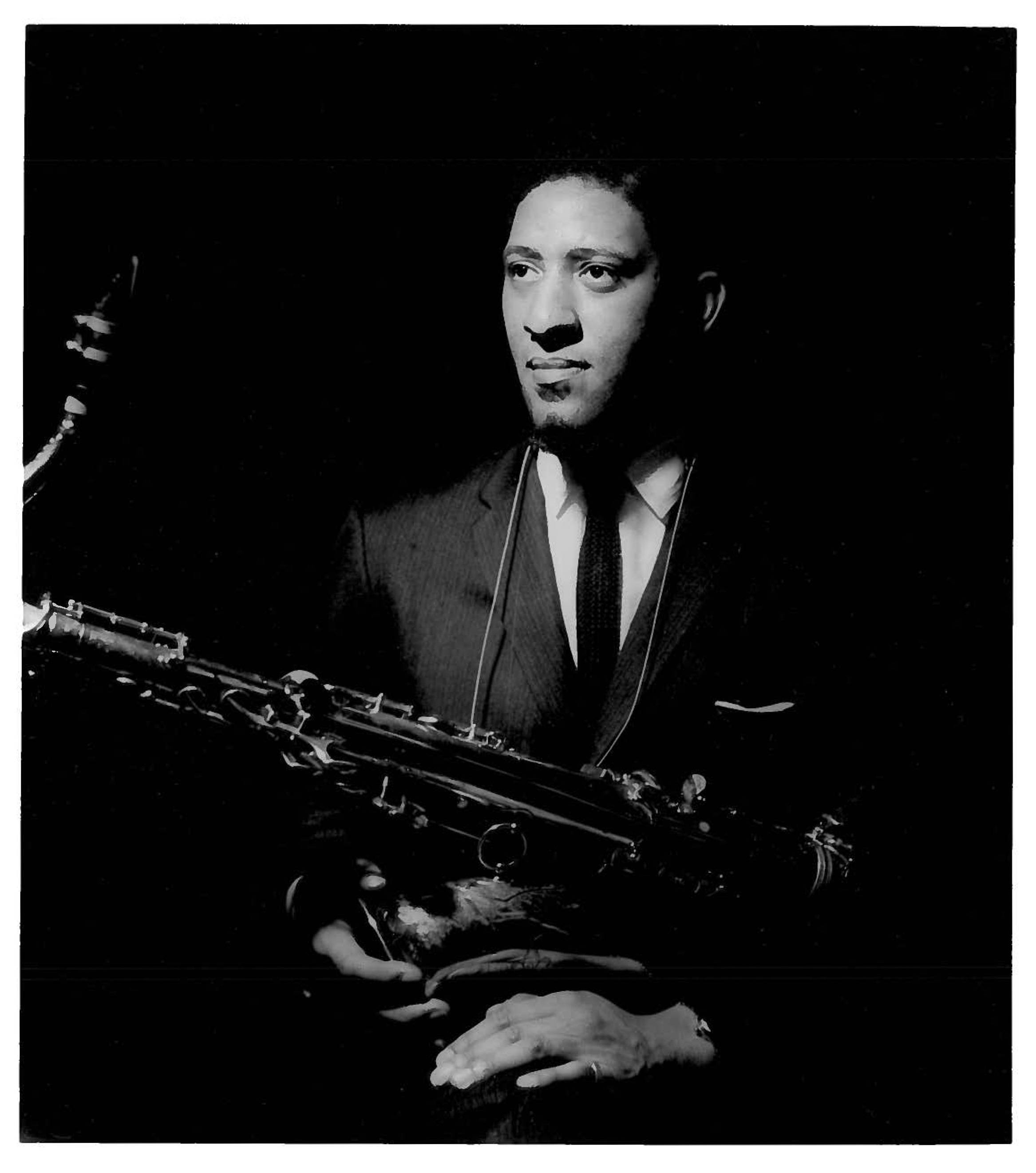 年輕的美國爵士音樂家 Sonny Rollins 壁紙 — 一個穿著西裝的男人在深色背景下拿著色士風的黑白肖像。