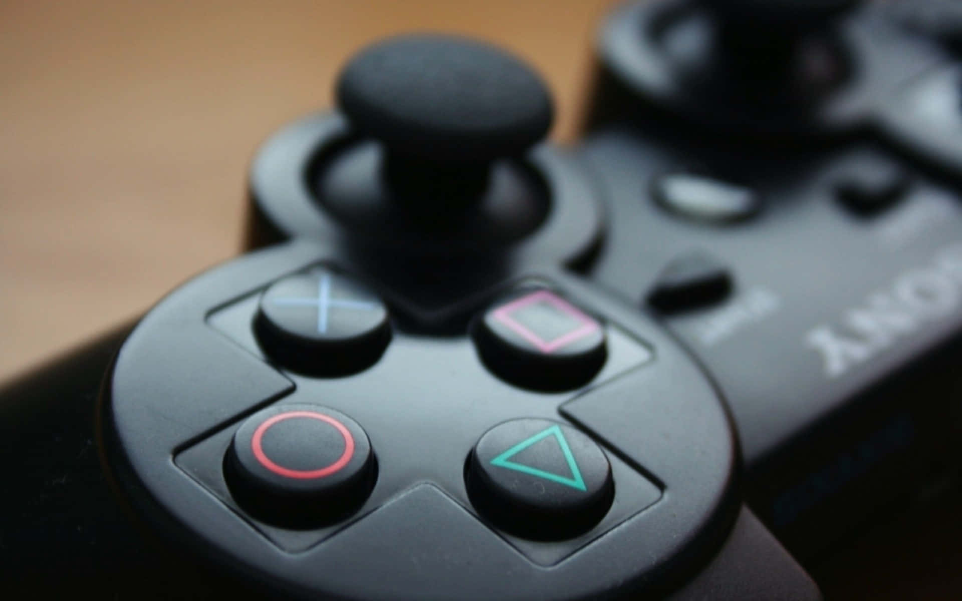 Sony PS3 遙控器按鈕 壁紙 — 黑色PlayStation控制器特寫，帶有發光彩色按鈕，置於木質表面上。