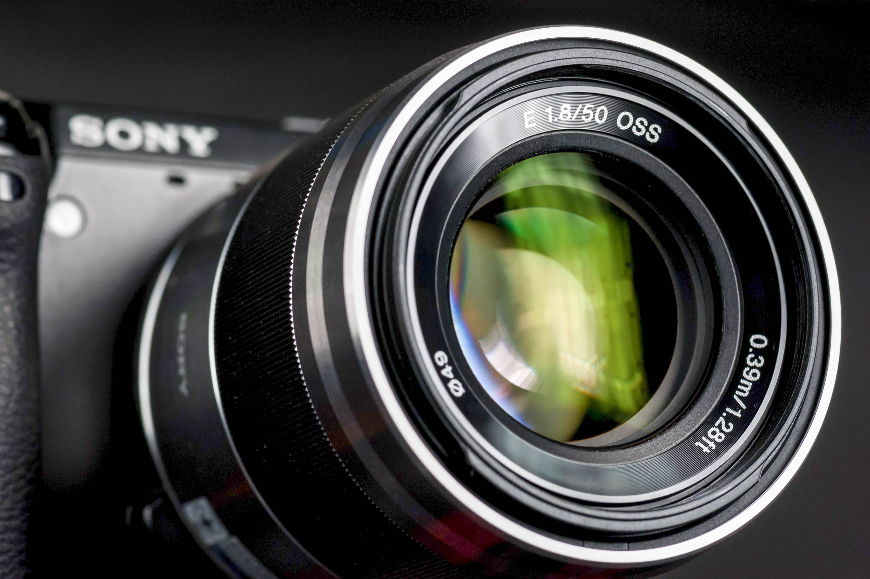 Sony相機NEX-7攝影產品 壁紙 — Sony相機鏡頭特寫，玻璃上有可見文字和模糊的綠色反射。