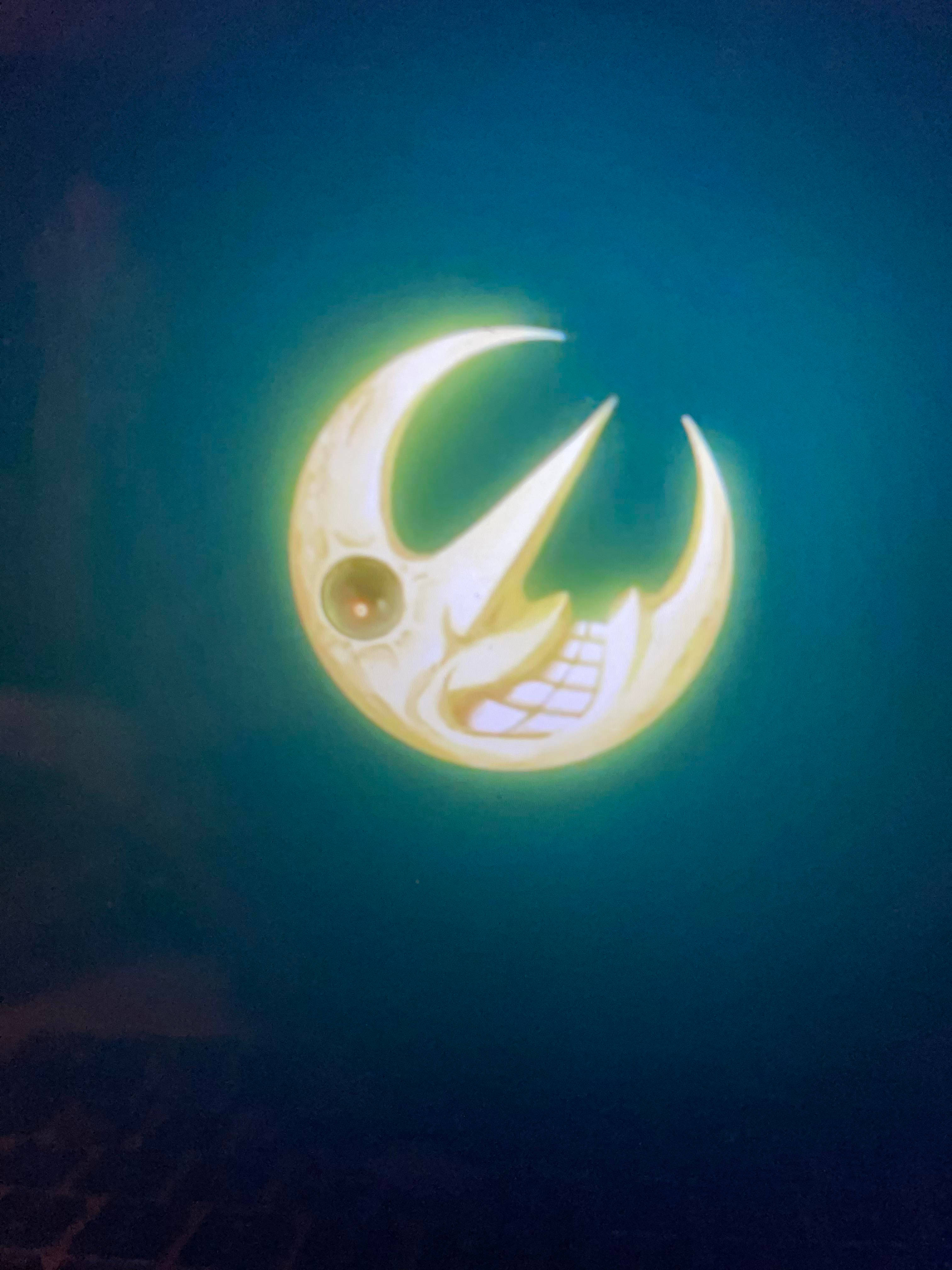 Soul Eater 月在深藍背景 壁紙 — 一個發光的彎月，帶有卡通臉和尖銳的牙齒，在深青色背景上明亮地閃耀。