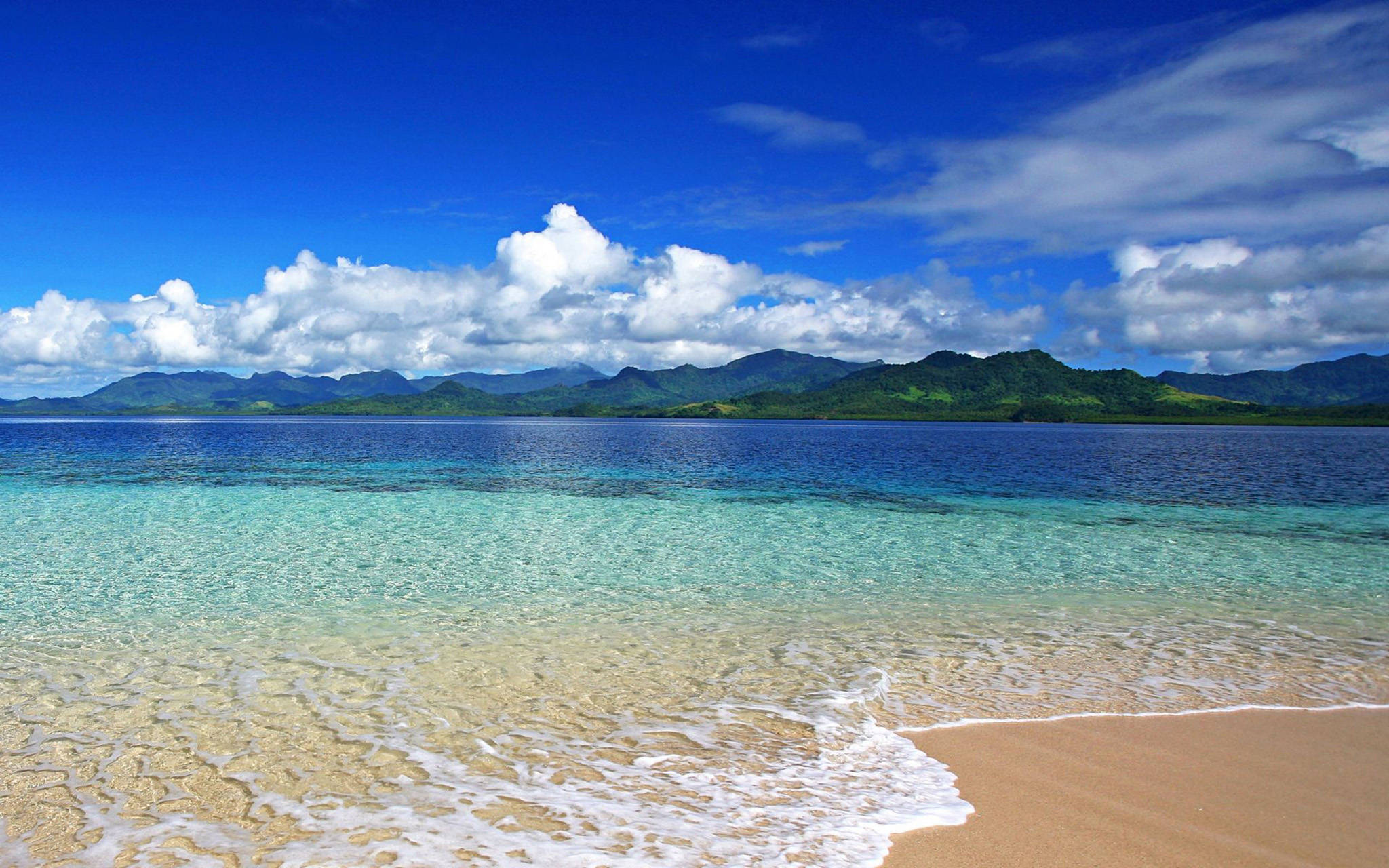 South Pacific Ocean View 壁紙 — 清澈的碧綠海水拍打著金色的沙灘，在湛藍的天空和蓬鬆的白雲下。