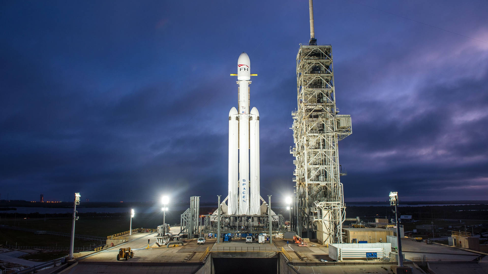 黃昏時分發射台上的SpaceX火箭，伴隨著戲劇性的雲彩和明亮的燈光。 — Spacex GIF 壁紙