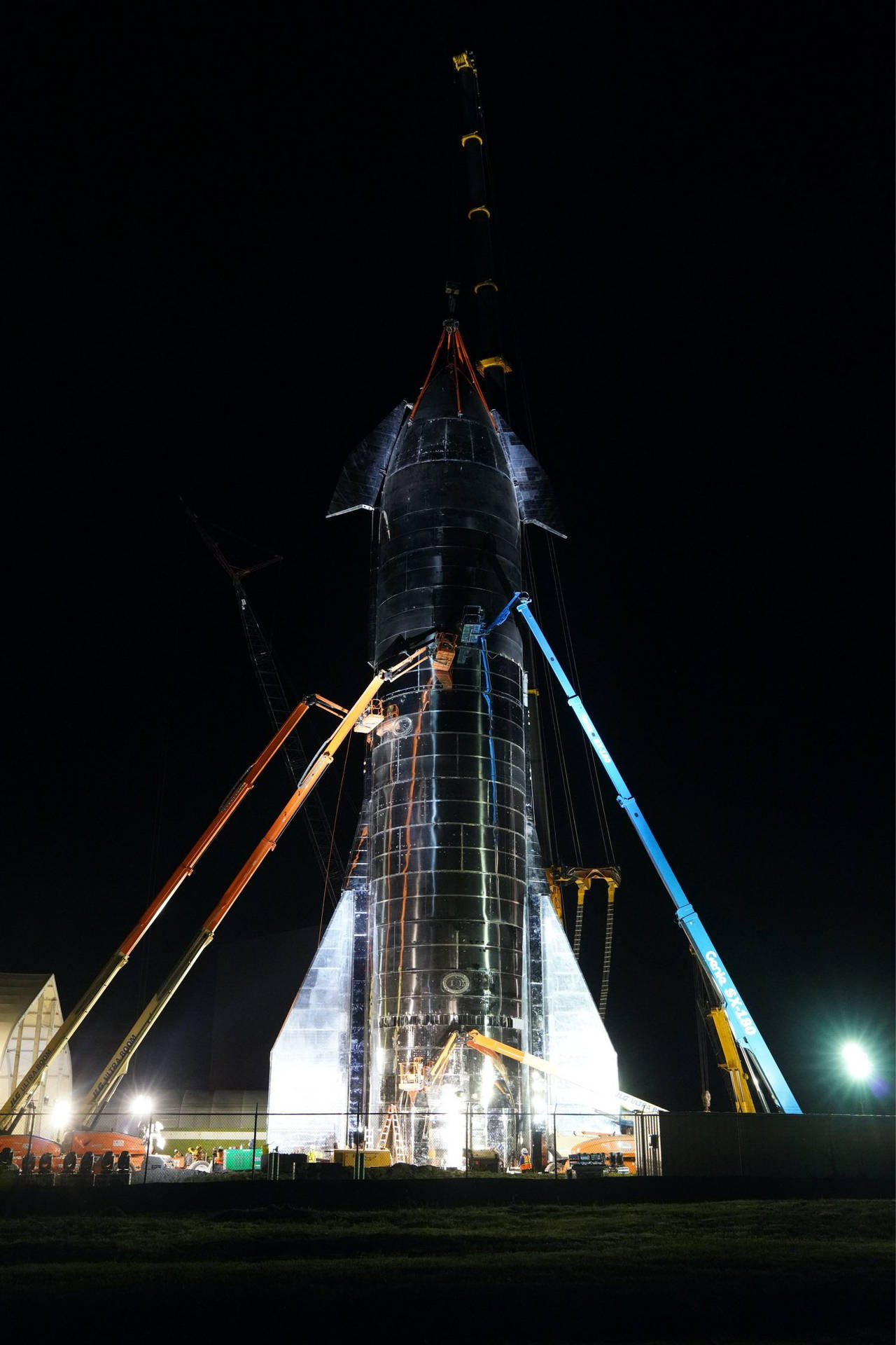 夜間組裝的大型火箭，周圍有起重機和工人。