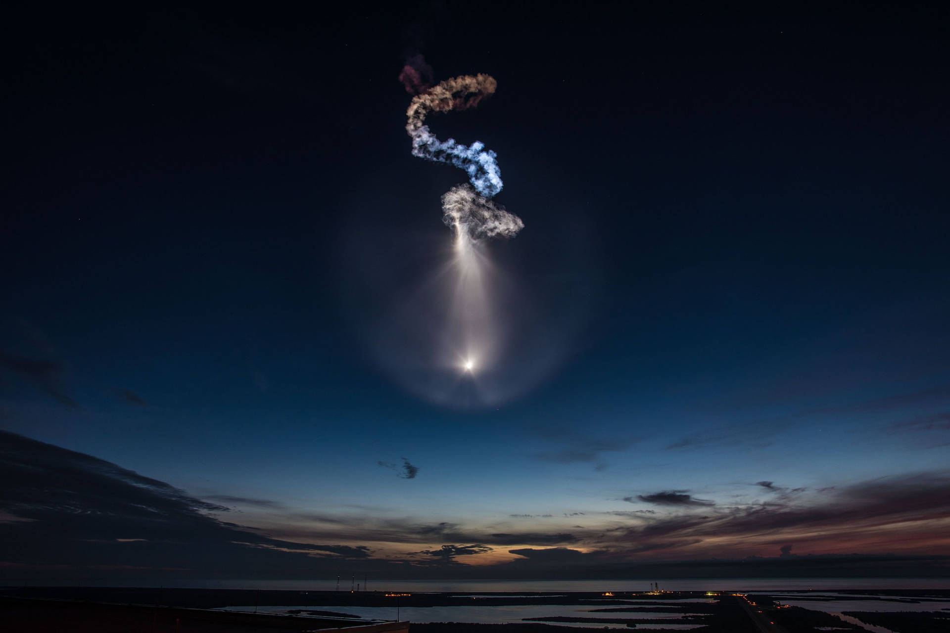 黃昏時的火箭發射，在暮色天空中留下發光軌跡和煙霧螺旋 — Spacex GIF 壁紙