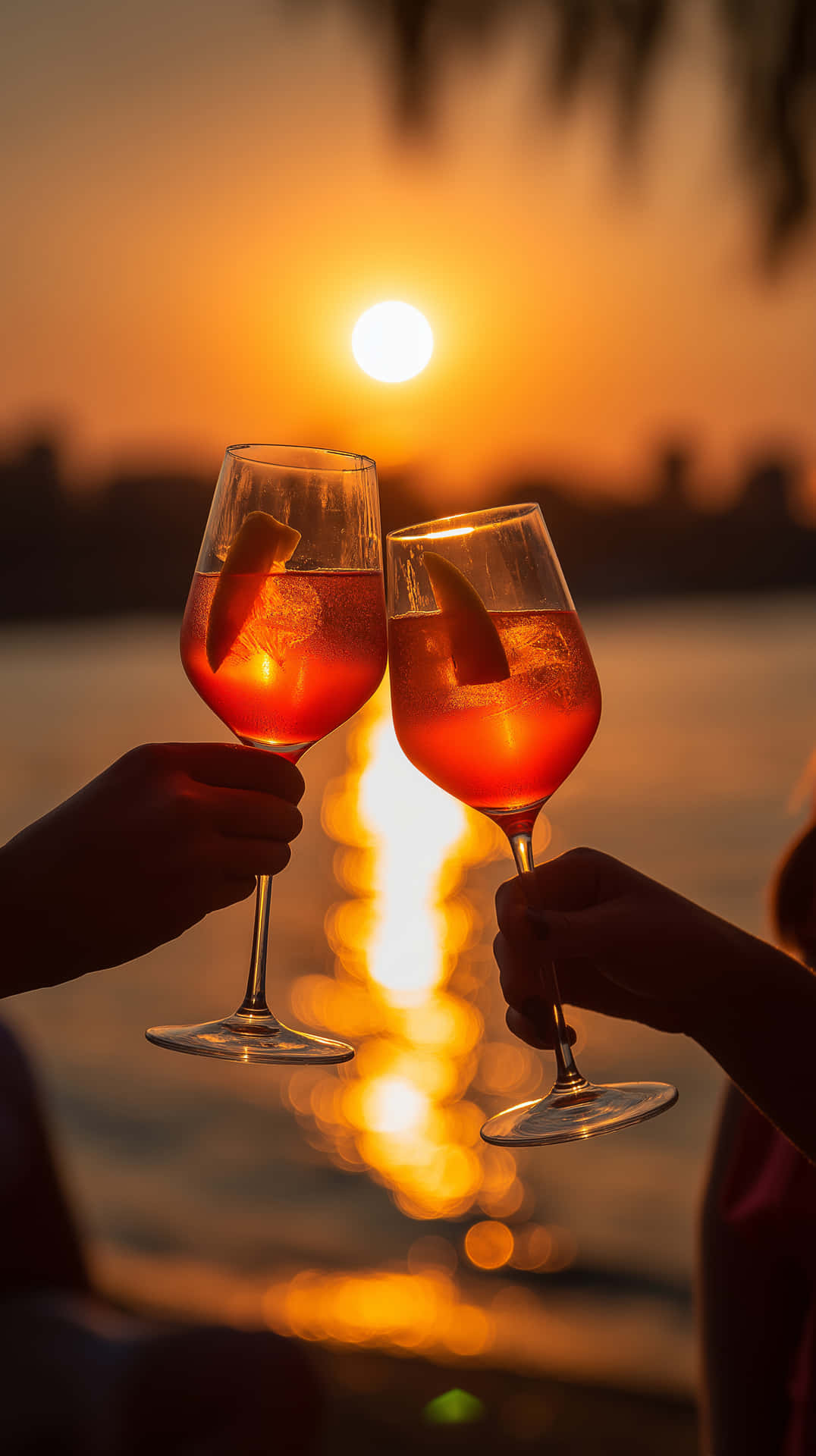 兩隻手喺水面夕陽下用橙色雞尾酒乾杯，上面有棕櫚葉。