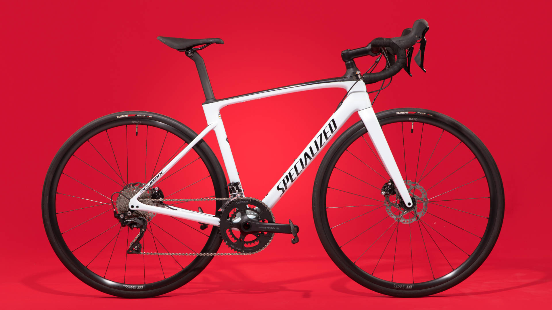 白色 Specialized 自行車 壁紙 — 一架時尚的白色Specialized公路單車，帶有黑色點綴，矗立在搶眼的紅色工作室背景前。