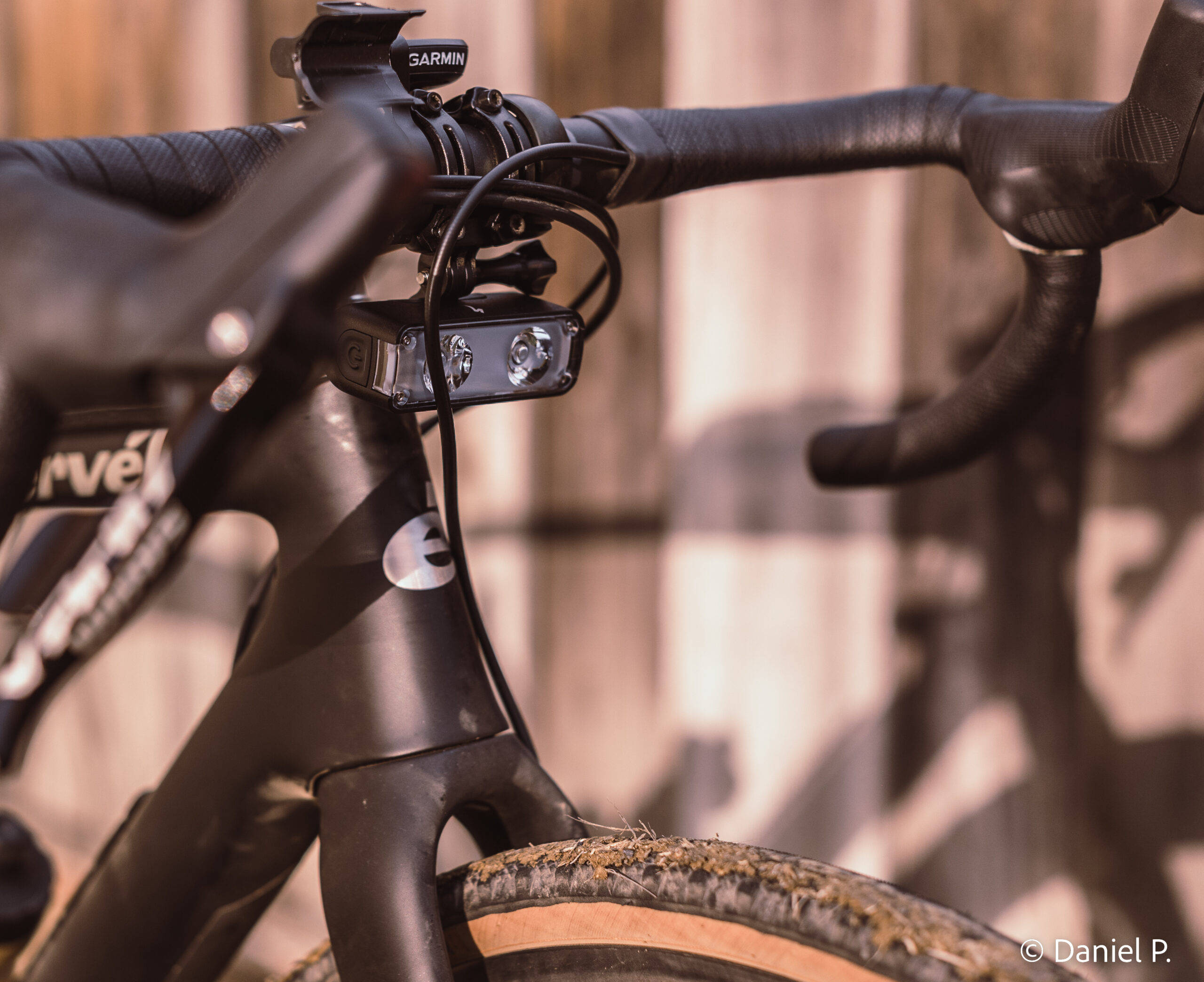 騎士駕馭 Specialized 自行車穿行森林小徑 壁紙 — 特寫鏡頭：時尚黑色單車把手，配備 Garmin 碼錶及前燈，背景為模糊的木柵欄。