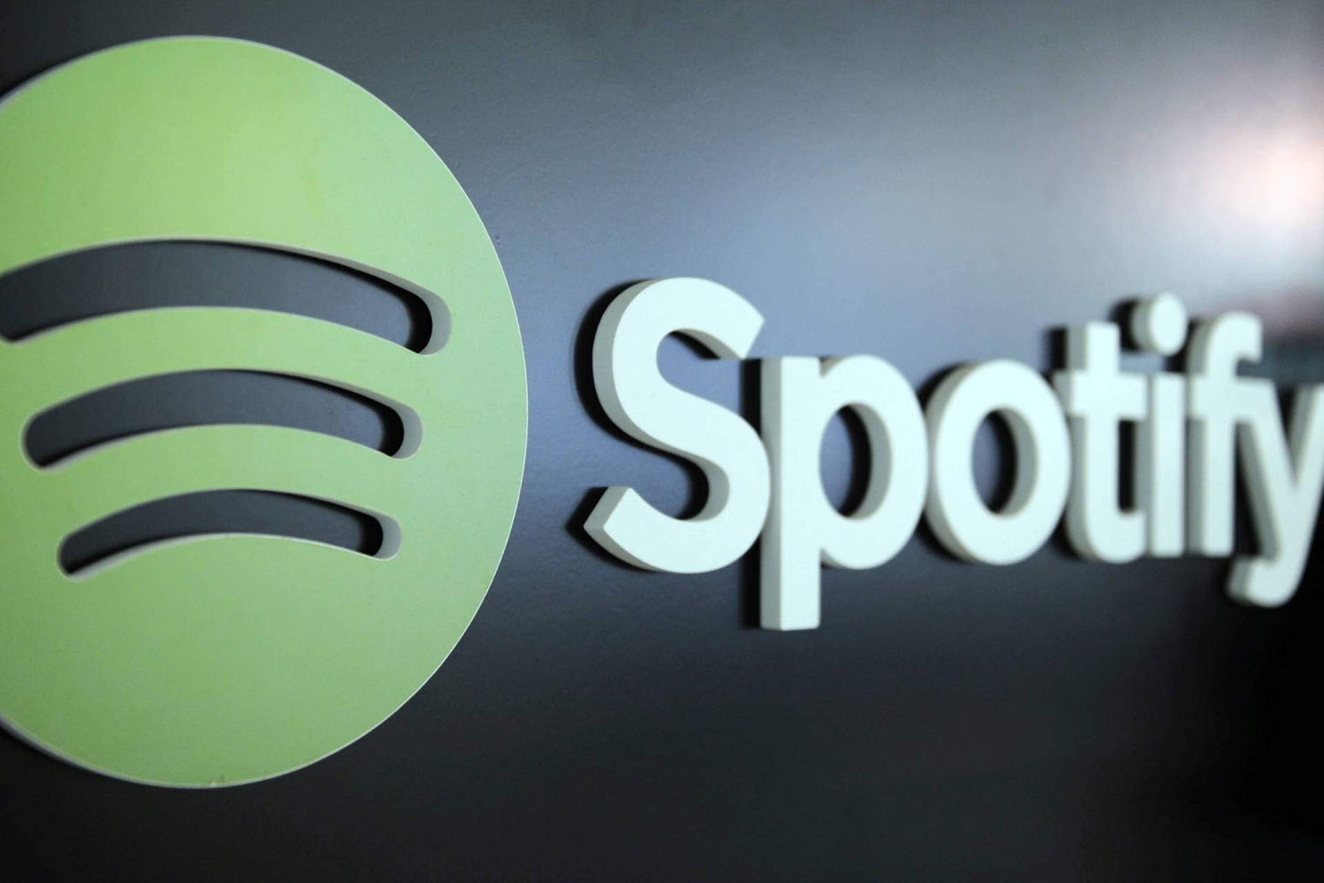 深色牆上帶有綠色圓圈和白色文字的Spotify標誌牌。