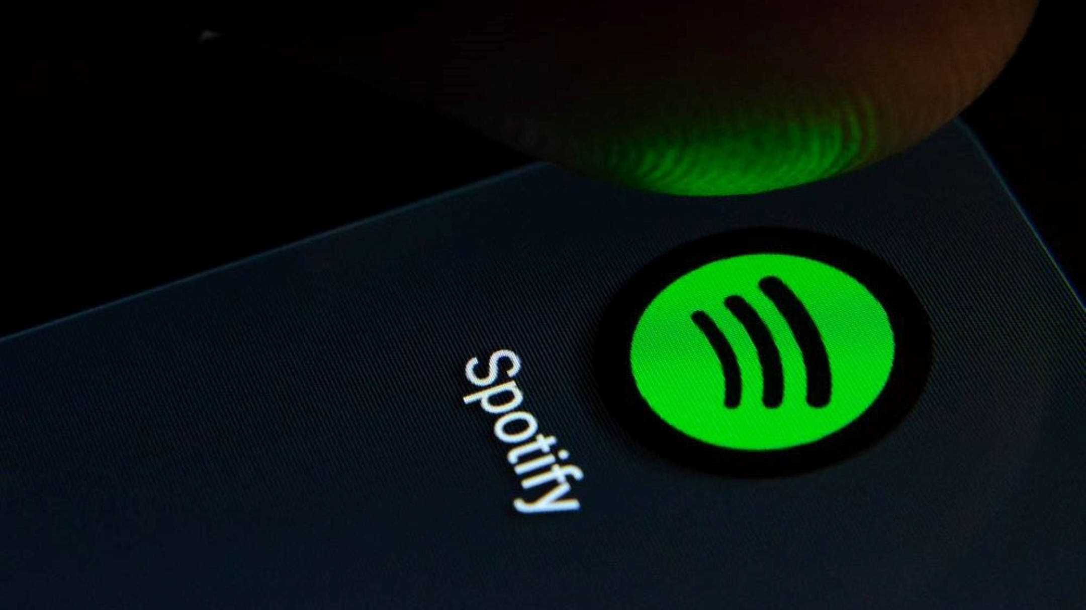 Spotify 屏幕顯示 壁紙 — 手指按壓黑暗智能手機屏幕上發光的綠色Spotify標誌的特寫。