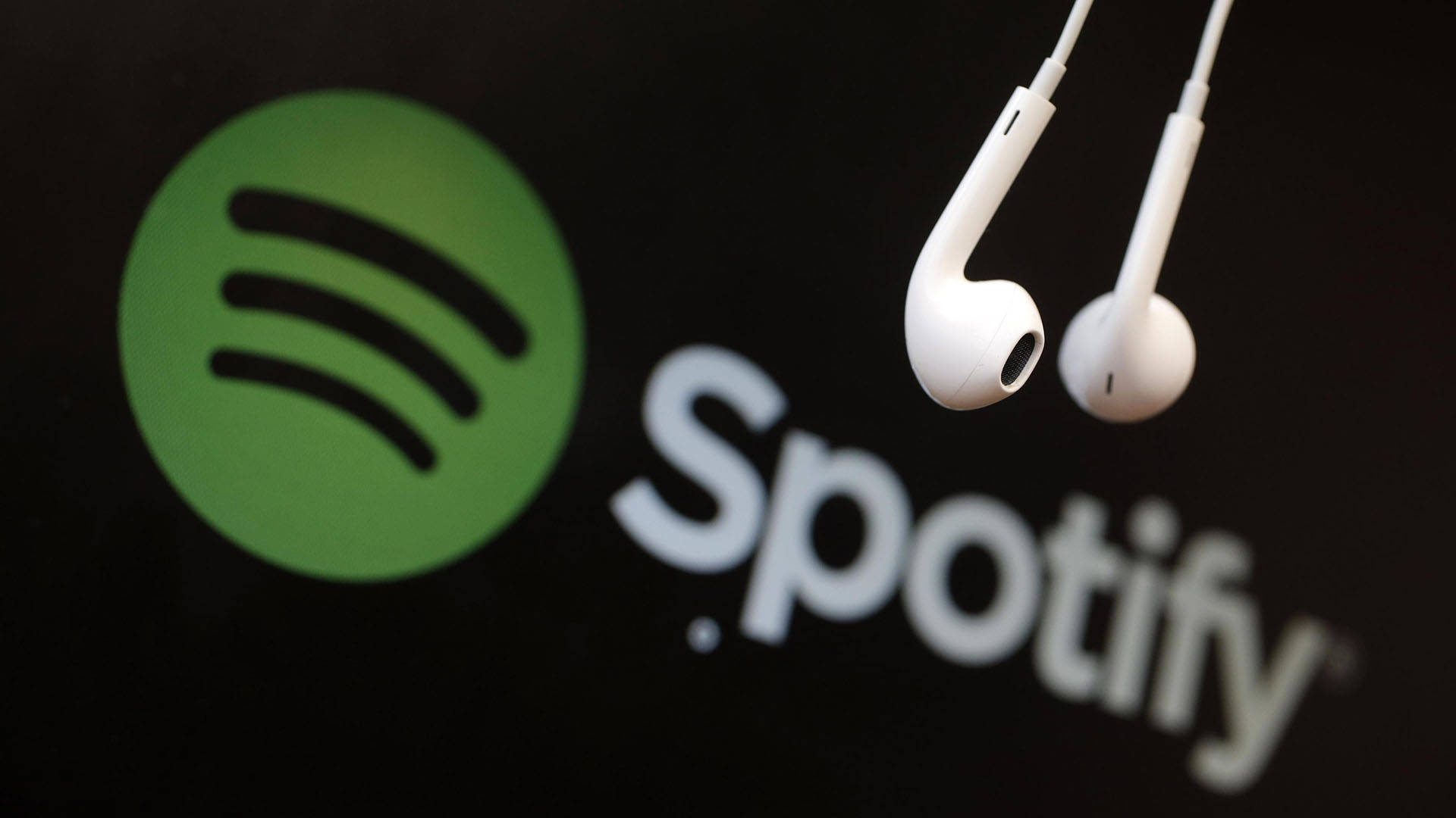 Spotify 標誌 Apple 壁紙 — 白色耳機懸掛在黑暗屏幕上發光的Spotify標誌上方。