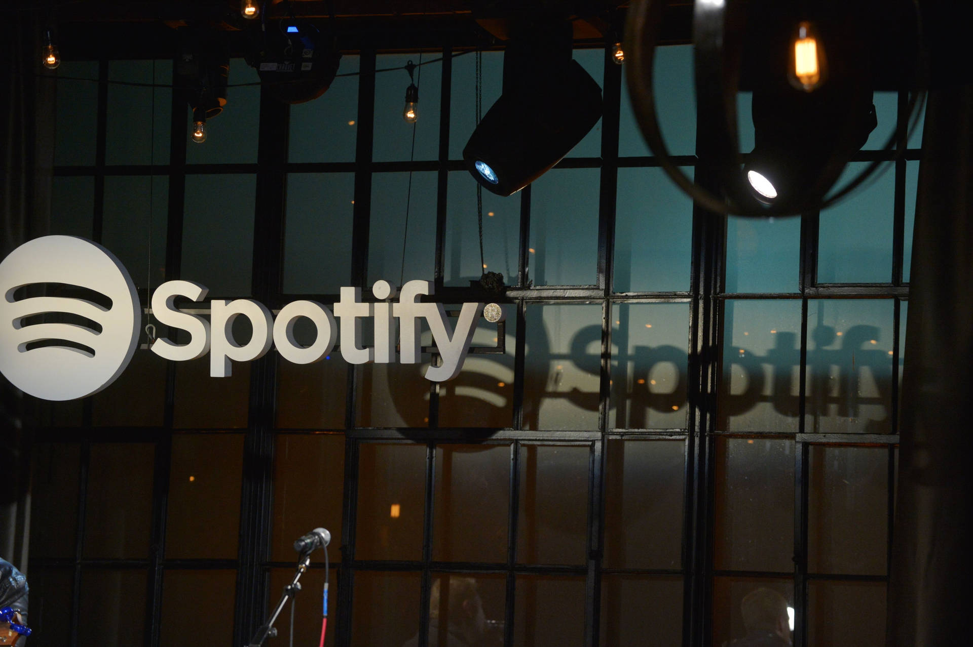 Spotify 標誌顯示在玻璃牆上，配有舞台燈光和咪高峰。