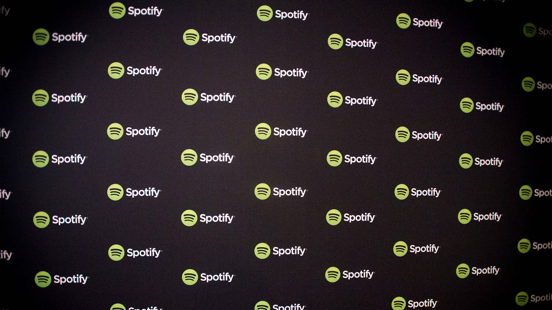 Spotify 黑色圖案壁紙 壁紙 — 一面深色牆壁，覆蓋著重複的Spotify標誌，帶有綠色圓圈和白色文字。