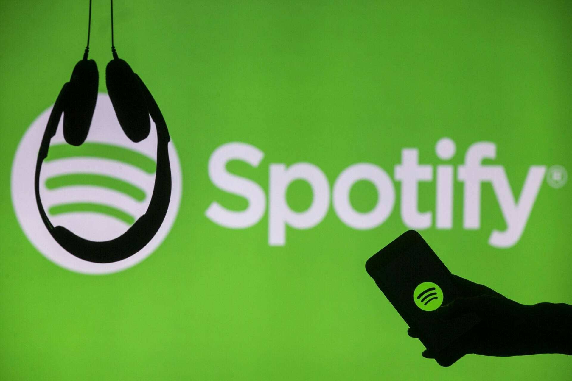 手部握著顯示Spotify標誌的手機，前方為綠色Spotify品牌背景，並有懸掛的耳機。