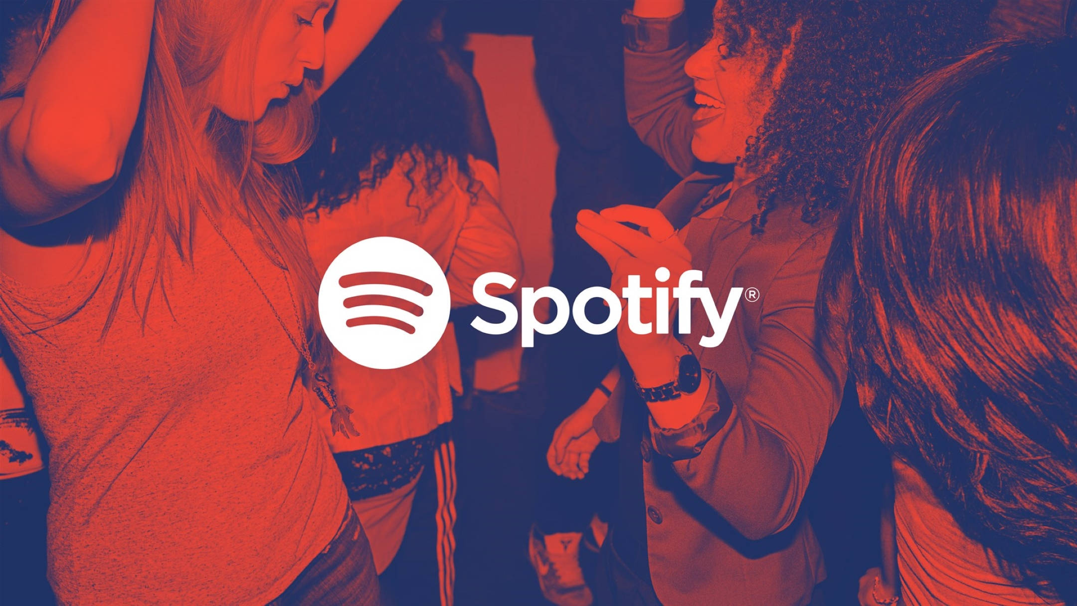 Spotify音樂舞動 壁紙 — 人們在燈光昏暗、帶有紅色和藍色燈光的俱樂部中跳舞，中央有Spotify標誌。