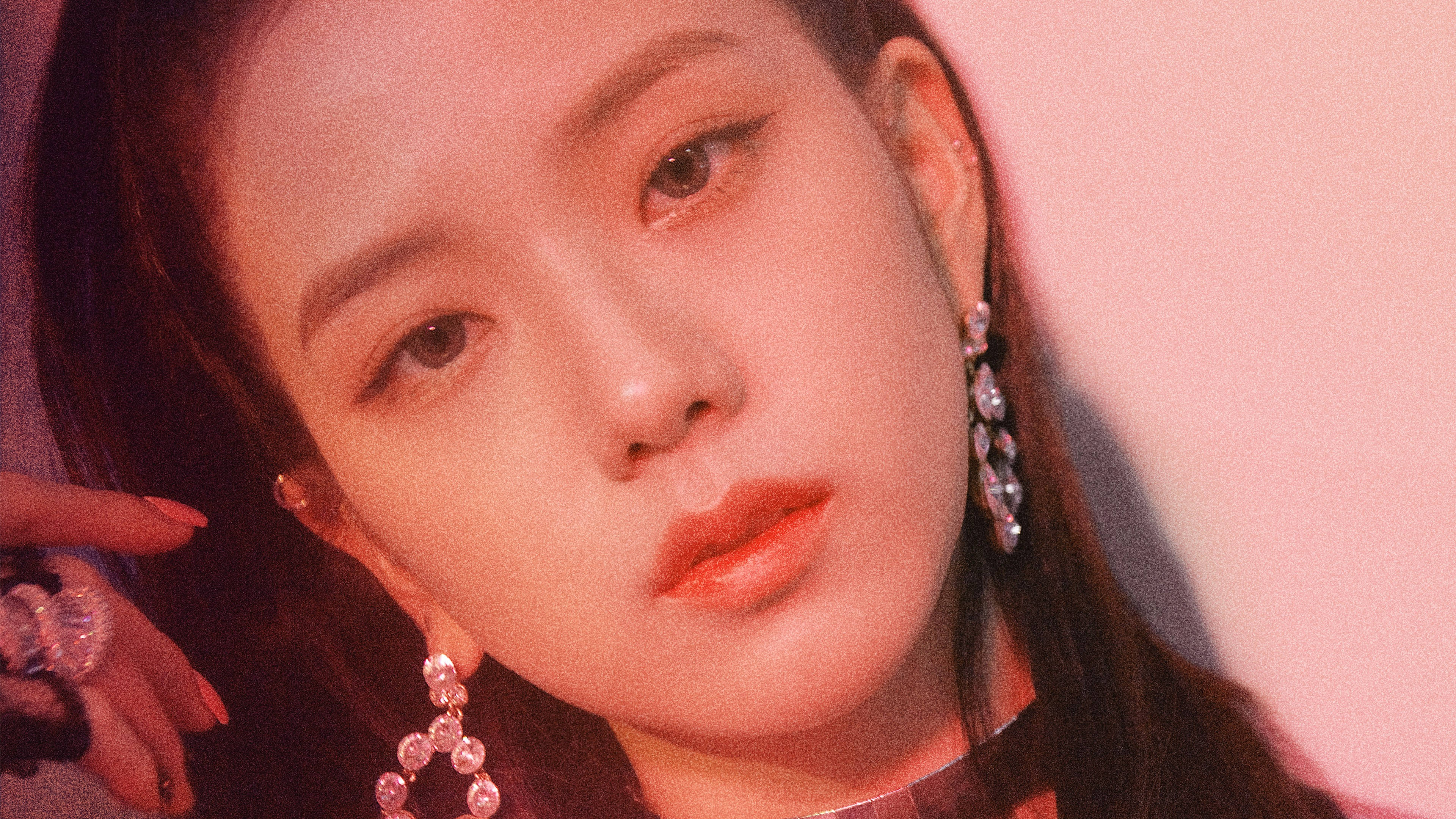 Square Up Jisoo寫真 壁紙 — 一位長黑髮女士在溫暖粉紅燈光下佩戴閃爍垂墜耳環和手錶的特寫肖像。
