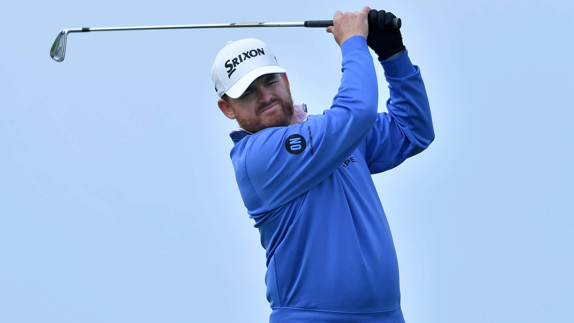 Srixon高爾夫球手Jb Holmes 壁紙 — 一名身穿藍色襯衫和白色帽子的男性高爾夫球手在晴朗的藍天下揮桿。