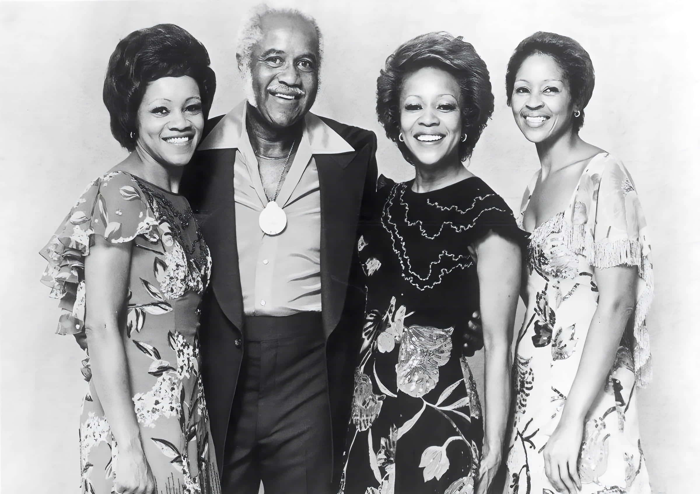 美國 Staple Singers 1970 年攝影棚拍攝 壁紙 — 四位微笑嘅人穿著復古花卉圖案及印花連衣裙，喺經典黑白影樓肖像中一齊擺姿勢。