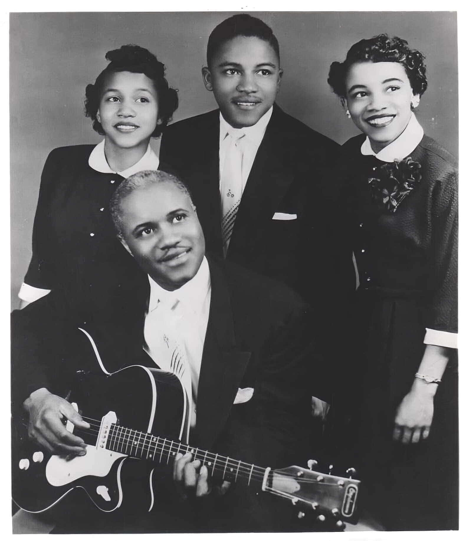 美國 Staple Singers 古董海報 壁紙 — 一張復古黑白工作室肖像照，四位微笑的非裔美國音樂家身著正裝，其中一人手持電結他。