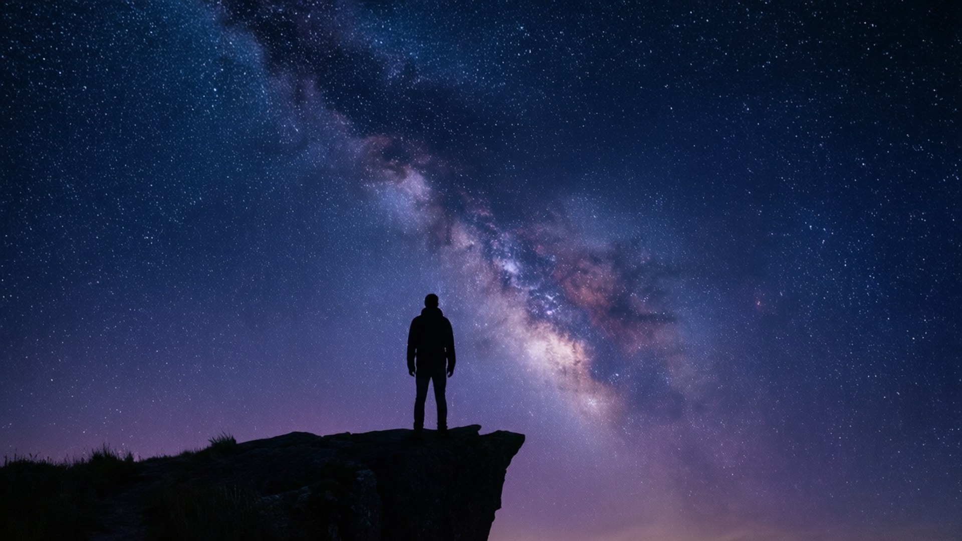夜晚在銀河系下的懸崖邊緣站立的人