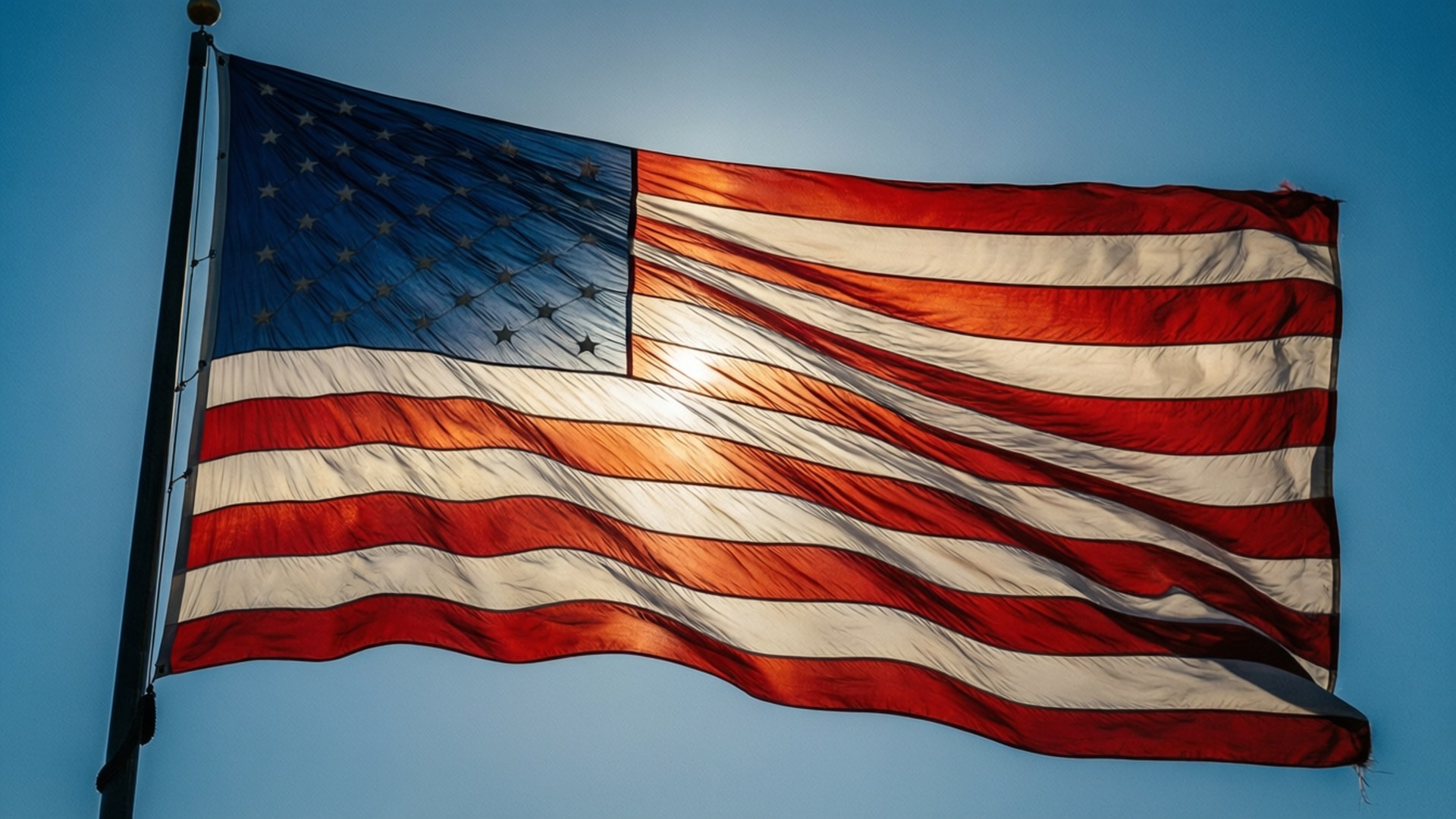 Stars and Stripes Sky 壁紙 — 美國國旗在晴朗的藍天下動態飄揚，陽光在紅、白、藍色的布料上閃爍。