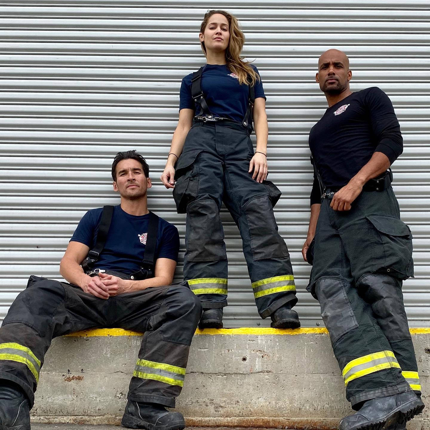 《Station 19》三人組 壁紙 — 三名全副裝備的消防員自信地擺姿勢，站在混凝土邊緣上，背景是波紋金屬牆。