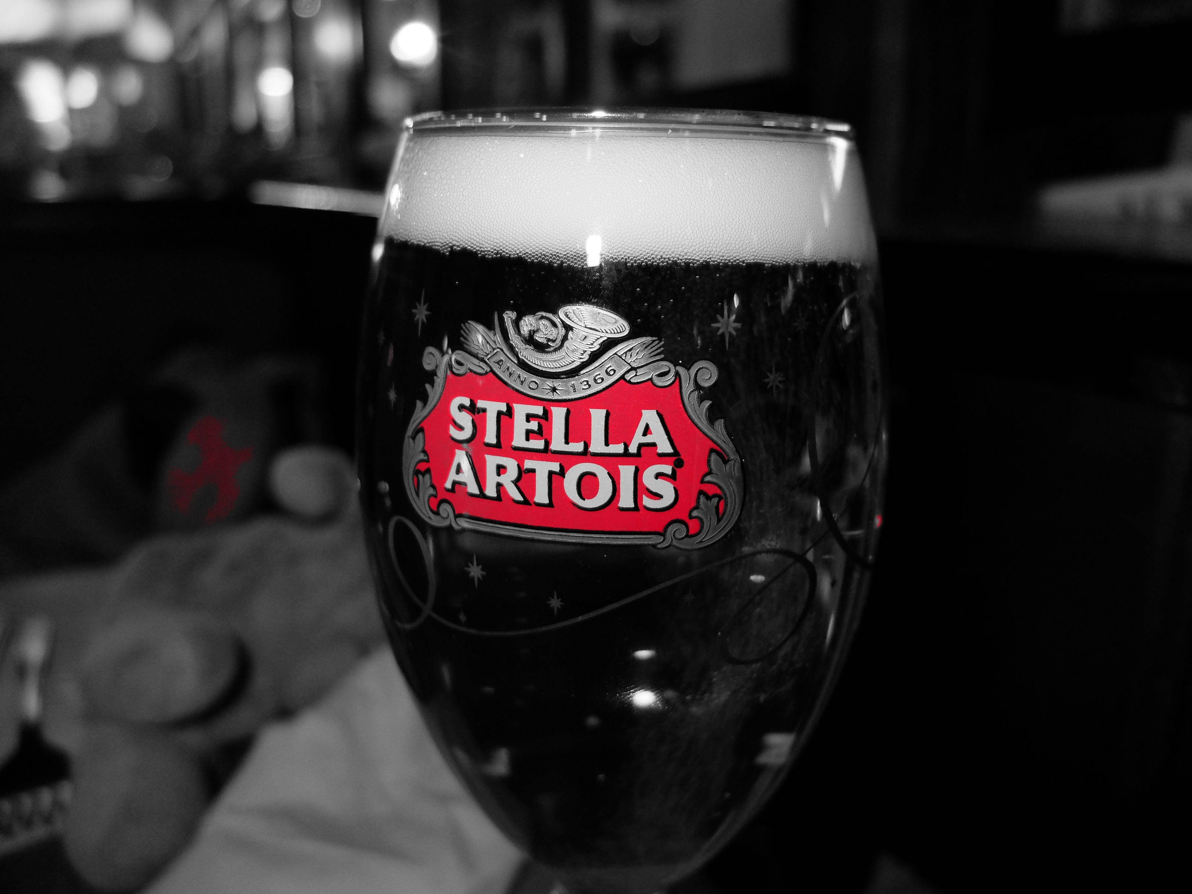 滿杯 Stella Artois 啤酒 壁紙 — 一個黑白特寫的Stella Artois啤酒杯，帶有鮮豔的紅色標誌和泡沫頂部，背景是模糊的酒吧。