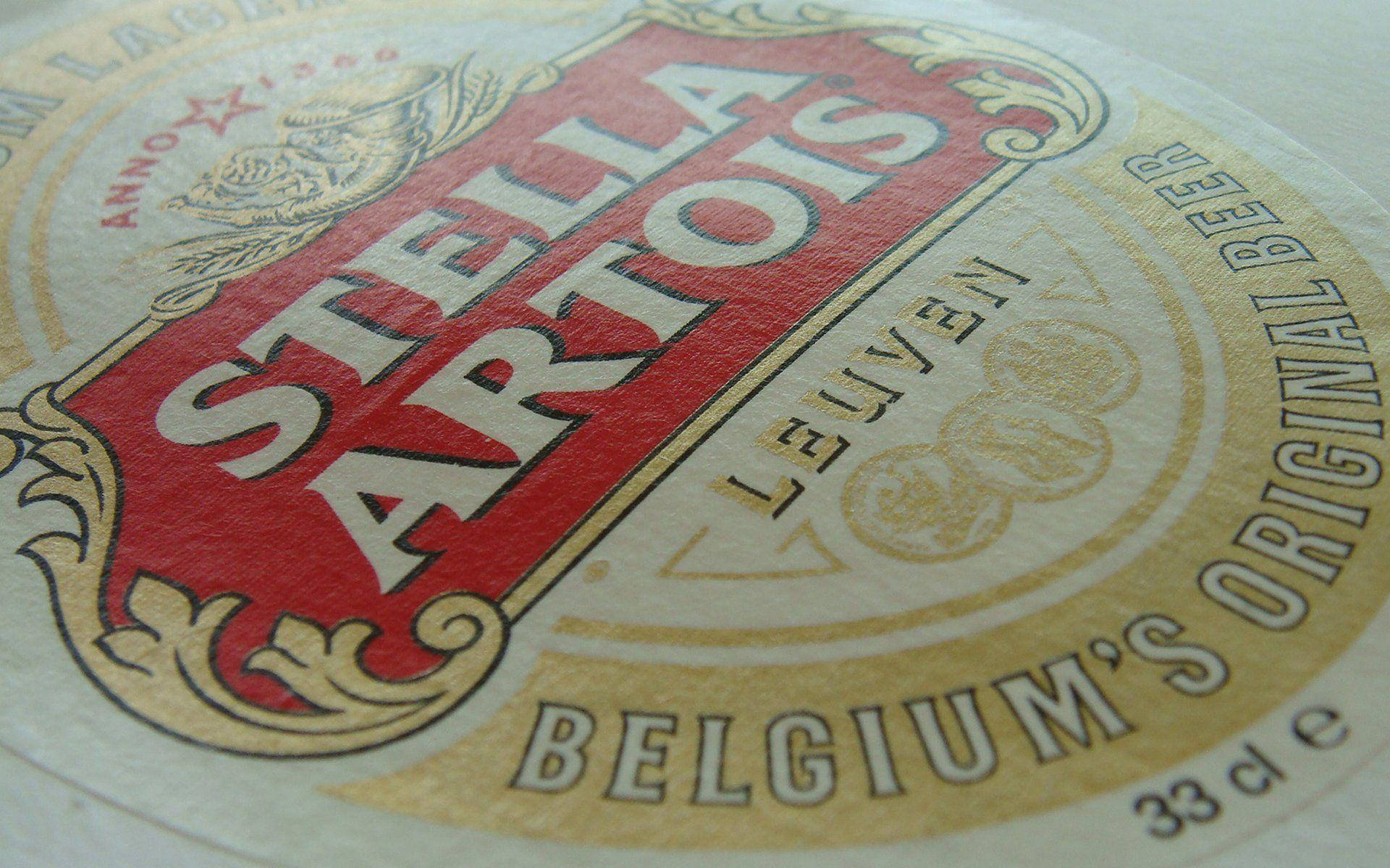 比利時原創啤酒 Stella Artois 壁紙 — Stella Artois 啤酒標籤的特寫，帶有紅色、金色和奶油色，展示複雜的復古字體和徽章設計。