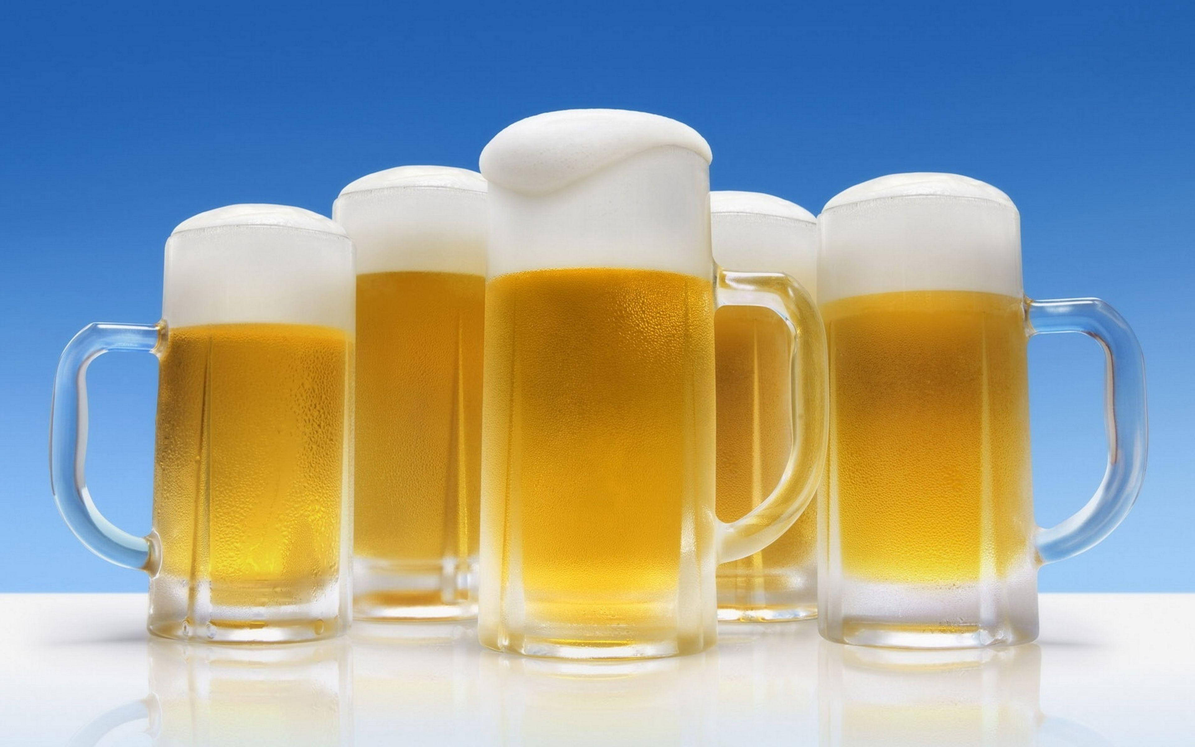 如比利時Stella Artois般金黃的啤酒 壁紙 — 五個冰凍啤酒杯，盛載著金黃色液體和白色泡沫，排列成一排，背景是充滿活力的藍色漸變。