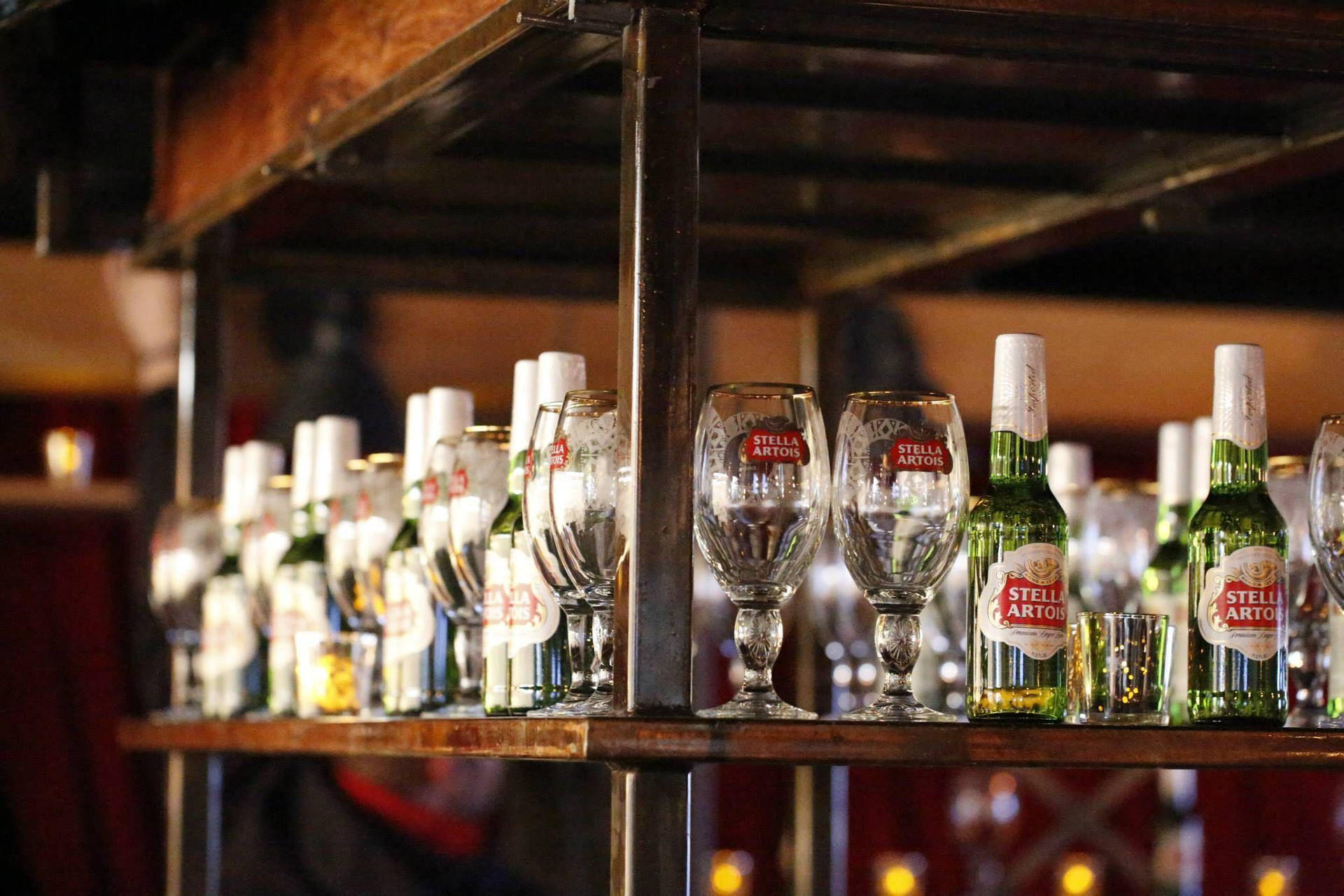 夜晚木製酒吧架上擺放的 Stella Artois 啤酒瓶和酒杯。