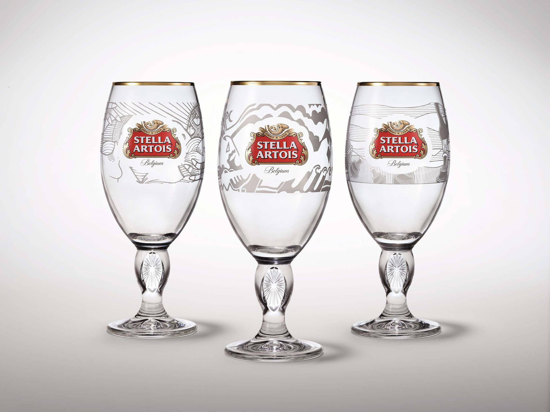三隻 Stella Artois 啤酒杯，帶有金色邊緣和蝕刻圖案，白色背景。