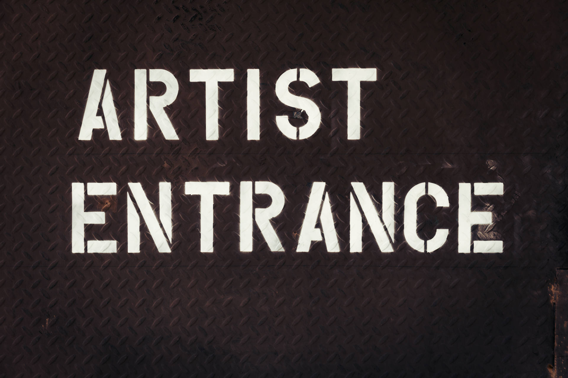 深色金屬紋理上白色模板的 artist entrance 標誌。