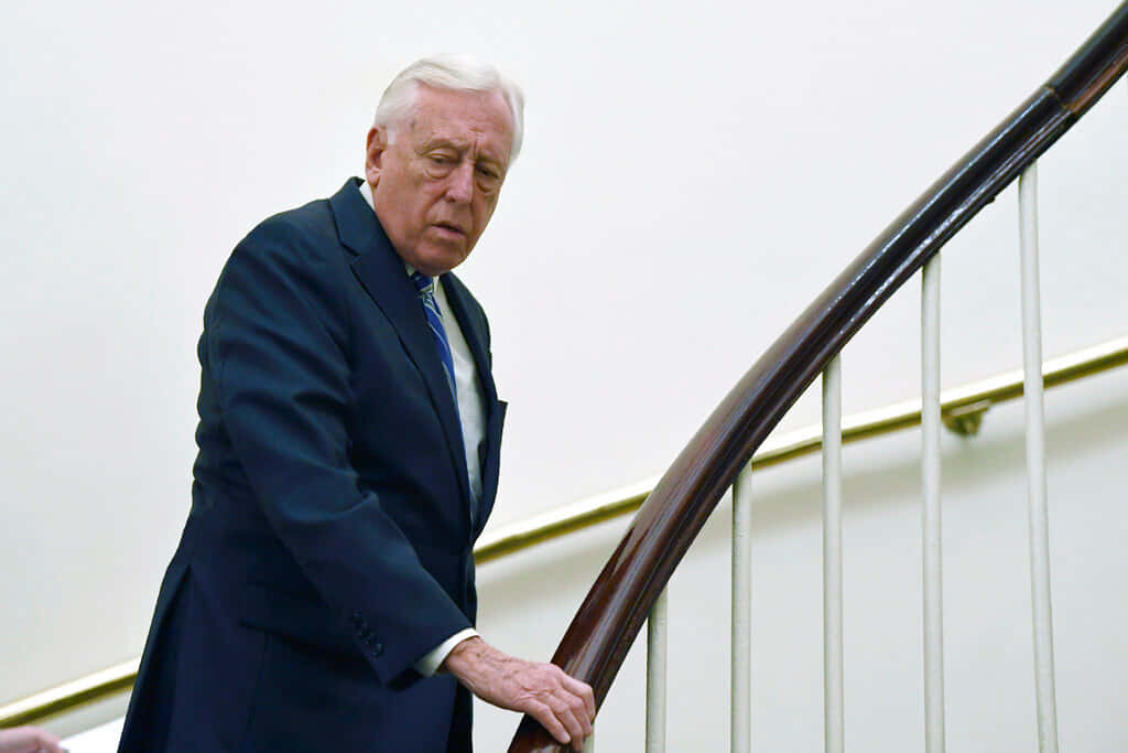 Steny Hoyer 正攀樓梯 壁紙 — 一位身穿深色西裝的長者小心翼翼地走下帶有白色欄杆的弧形木樓梯。