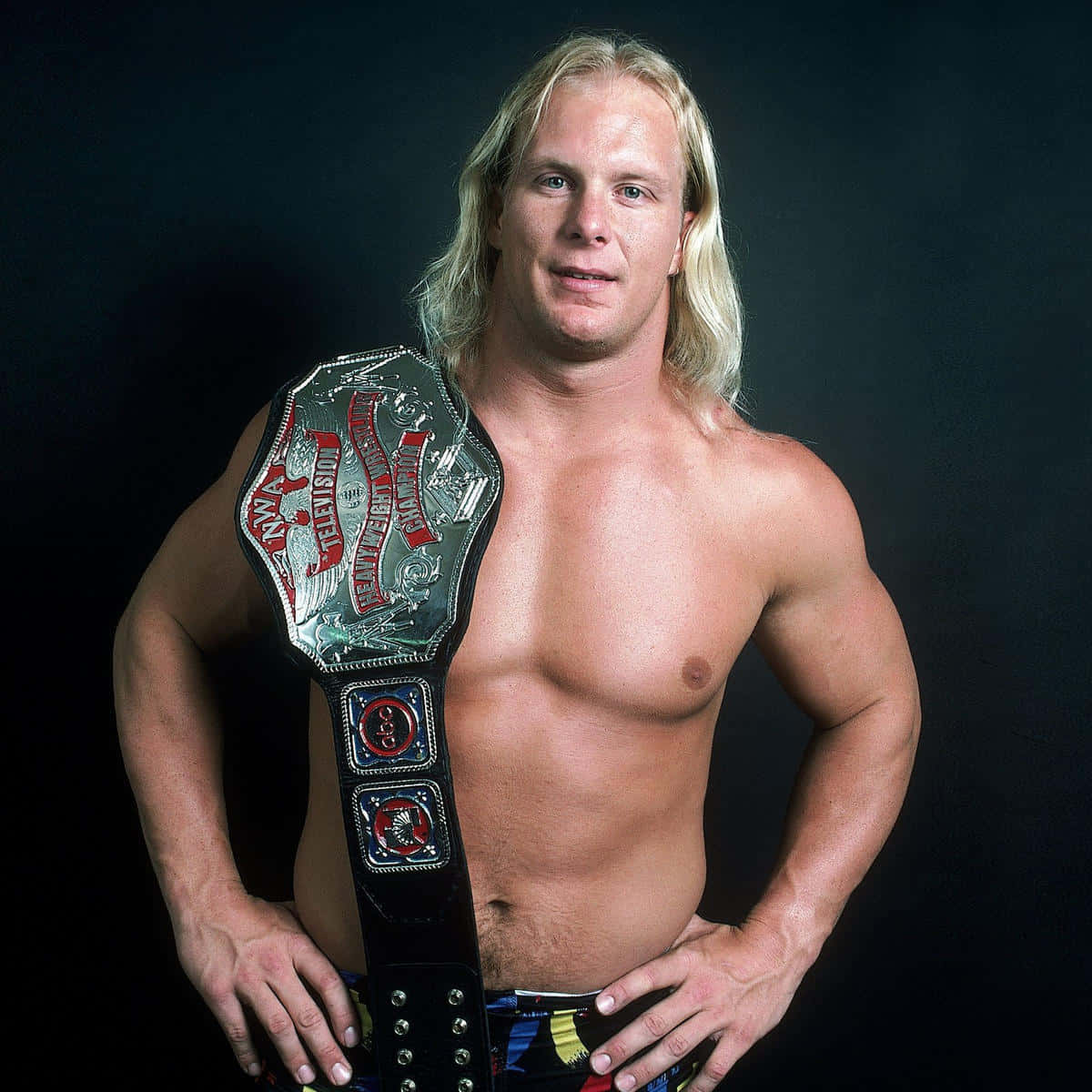 重量級摔角冠軍Steve Austin肖像 壁紙 — 一位肌肉發達的金髮摔角手，肩上掛著冠軍腰帶，在深色工作室背景下自信地擺姿勢。