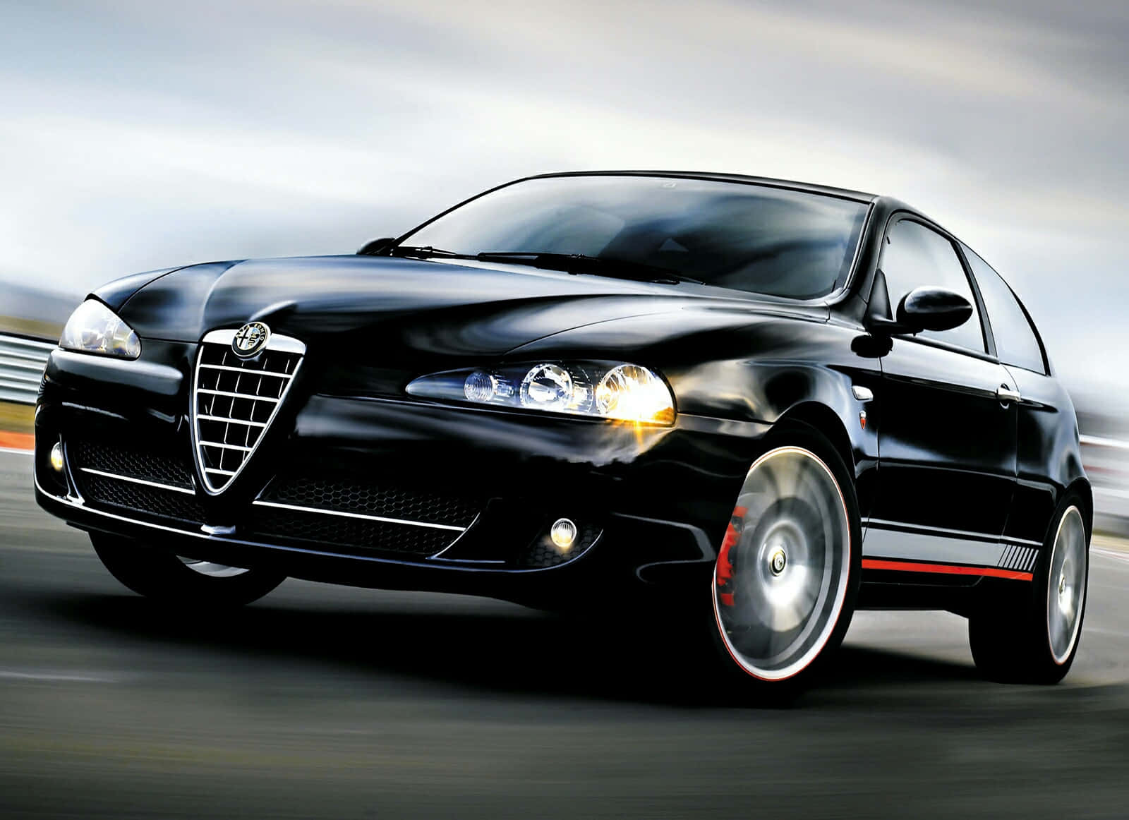 Alfa Romeo 147 桌布 壁紙 — 一輛時尚的黑色愛快羅密歐跑車在賽道上疾馳，帶有動態模糊和發光的車頭燈。