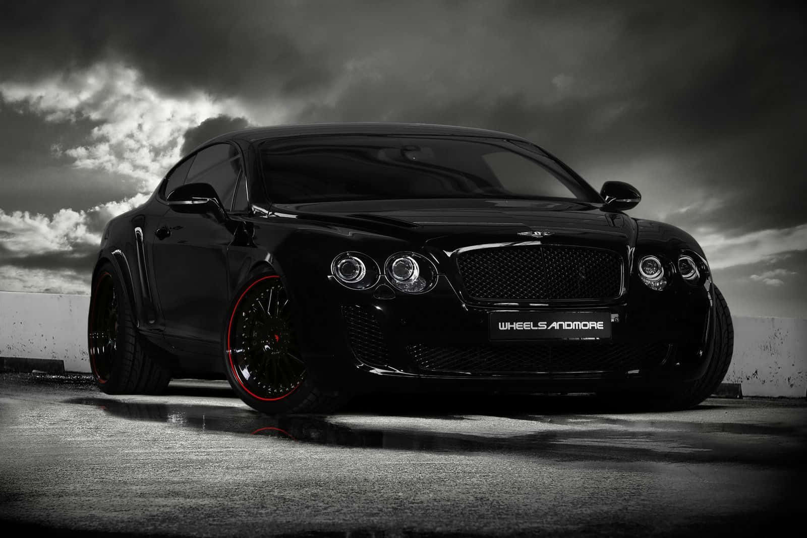 Bentley Continental Gt 桌布 壁紙 — 一輛時尚的黑色賓利 Continental GT 配備紅色輪圈，在戲劇性的暴風雨天空下停在濕漉漉的路面上。