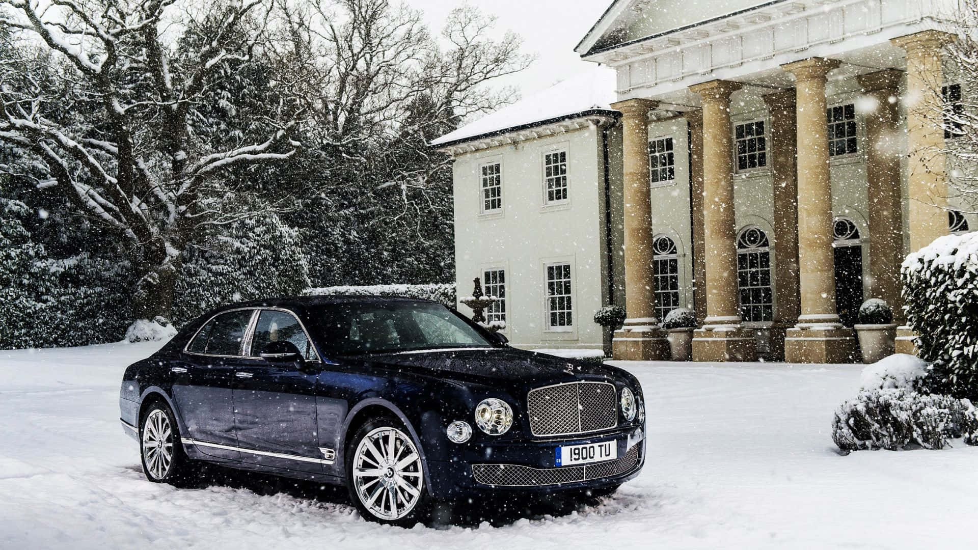 Bentley Mulsanne 桌布 壁紙 — 一架時尚的黑色賓利轎車停在新鮮雪地上，前方是宏偉的柱式豪宅，雪花飄落。