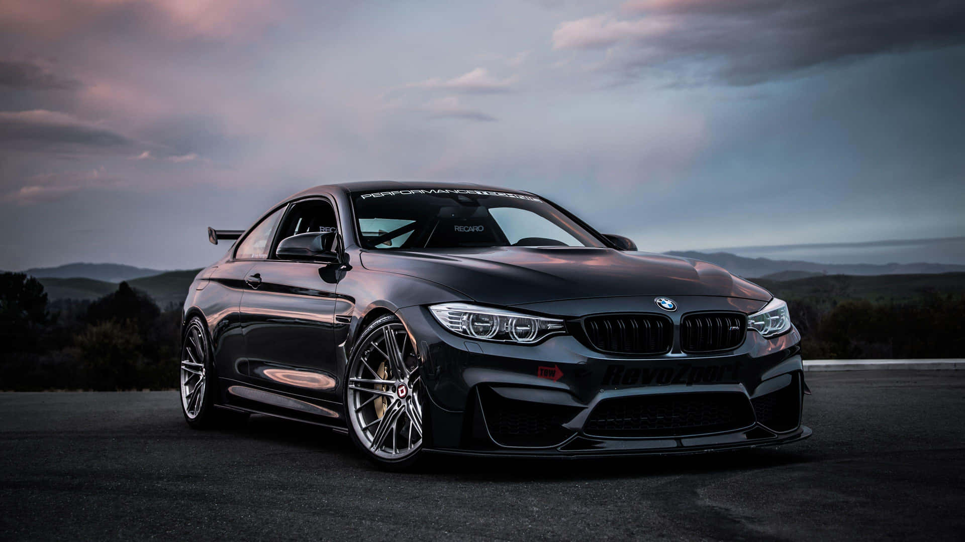 黑色BMW M4跑車停泊在黃昏時的路上，背景有山巒。