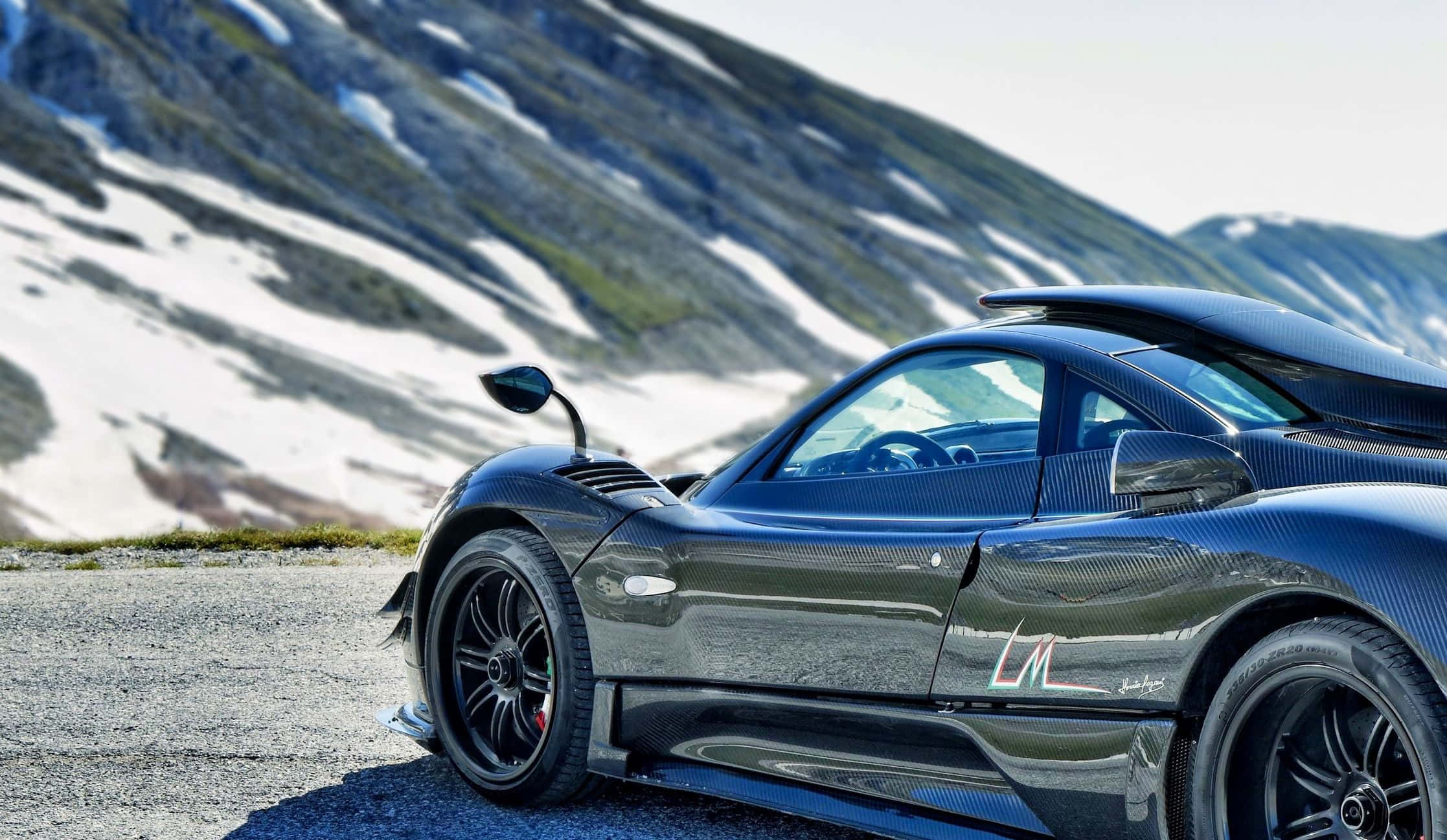 Pagani Zonda Hp Barchetta 桌布 壁紙 — 一架時尚的黑色碳纖維跑車停泊在碎石路上，背景是白雪覆蓋的山脈。