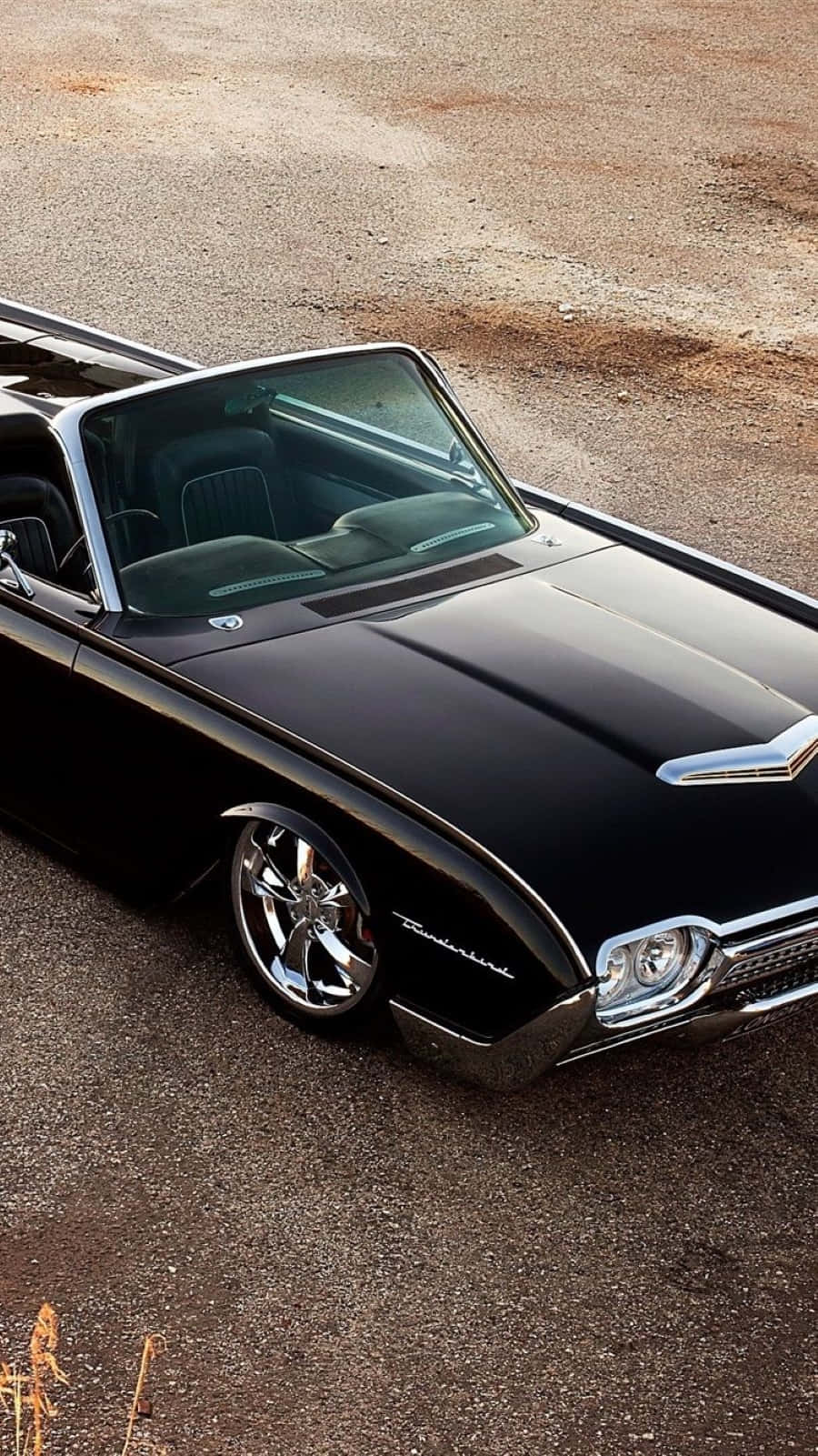 Ford Thunderbird 桌布 壁紙 — 一輛時尚的黑色經典敞篷跑車，帶有鍍鉻裝飾，停在礫石表面上，在明亮的日光下。