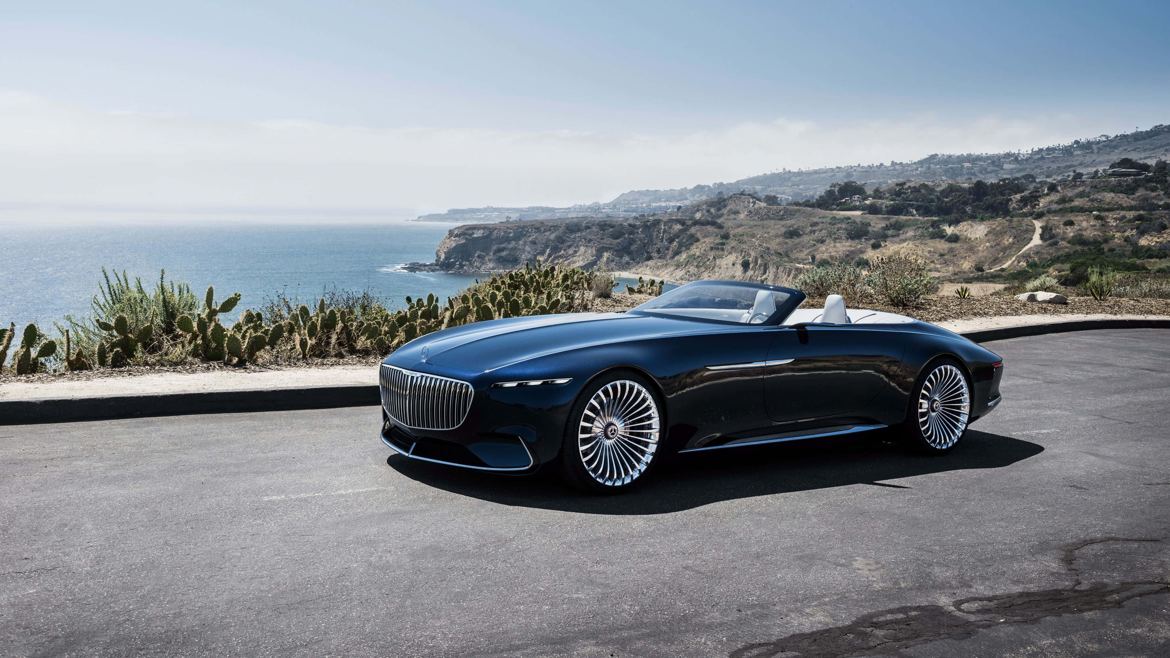 Maybach 桌布 壁紙 — 一架時尚黑色開篷跑車停泊在沿海公路上，俯瞰海洋，背景有仙人掌和懸崖。