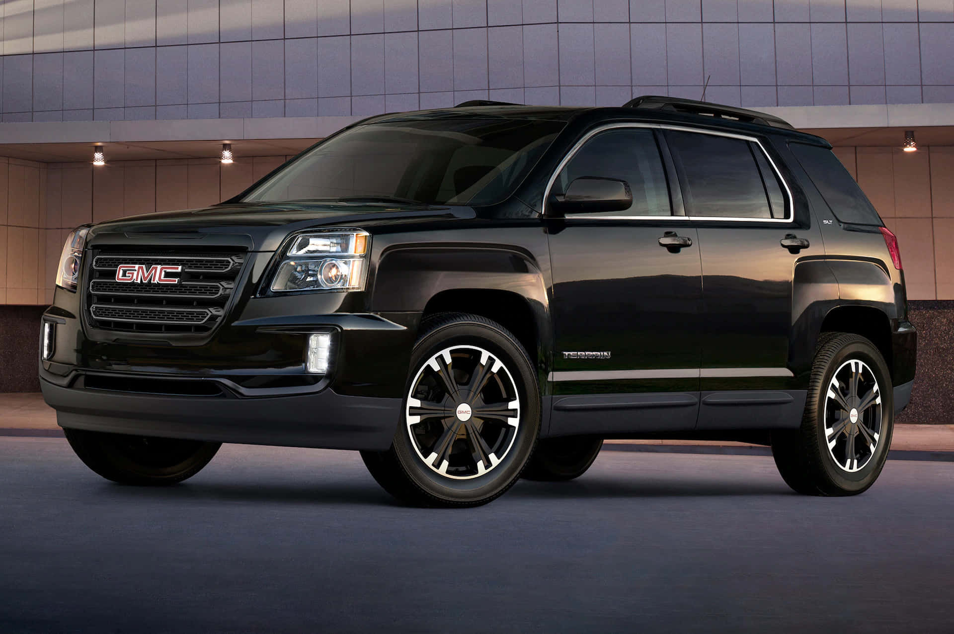 Gmc Terrain 桌布 壁紙 — 一輛時尚的黑色GMC Terrain SUV停在一棟現代建築前，伴隨著溫暖的晚間燈光。