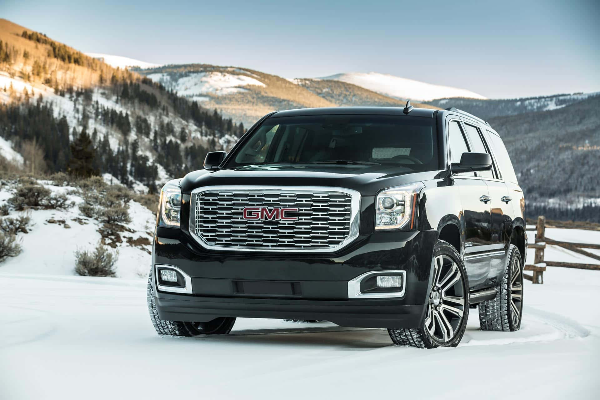 Gmc Yukon 桌布 壁紙 — 一架時尚的黑色GMC Yukon SUV停在積雪的山路上，背景是白雪覆蓋的山峰和常青樹。