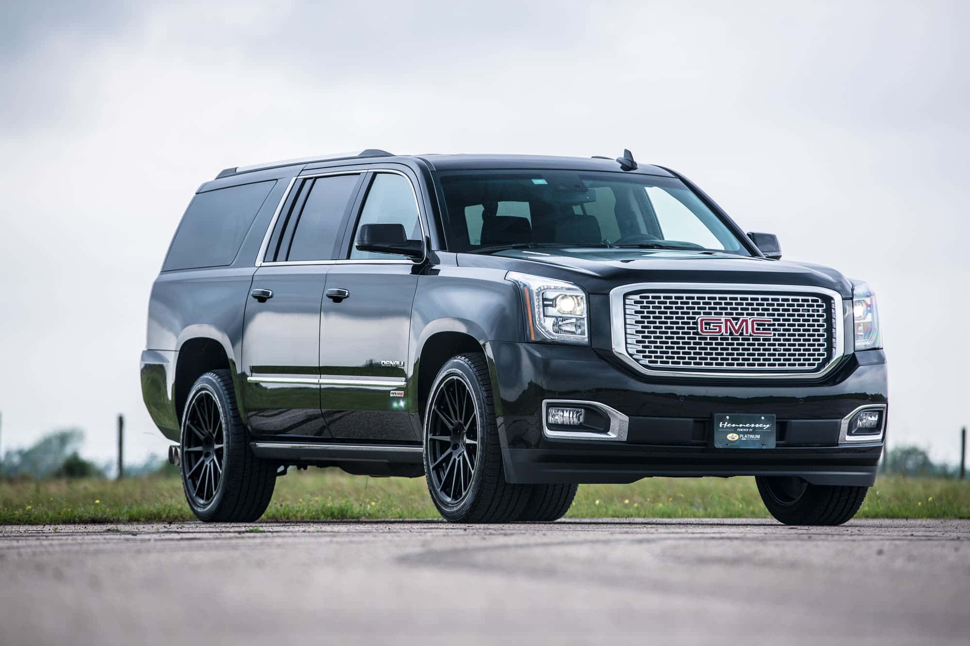 Gmc Yukon 桌布 壁紙 — 一架時尚的黑色GMC Yukon XL SUV，配備定制黑色輪圈，停泊在鋪砌道路上，背景是陰天。